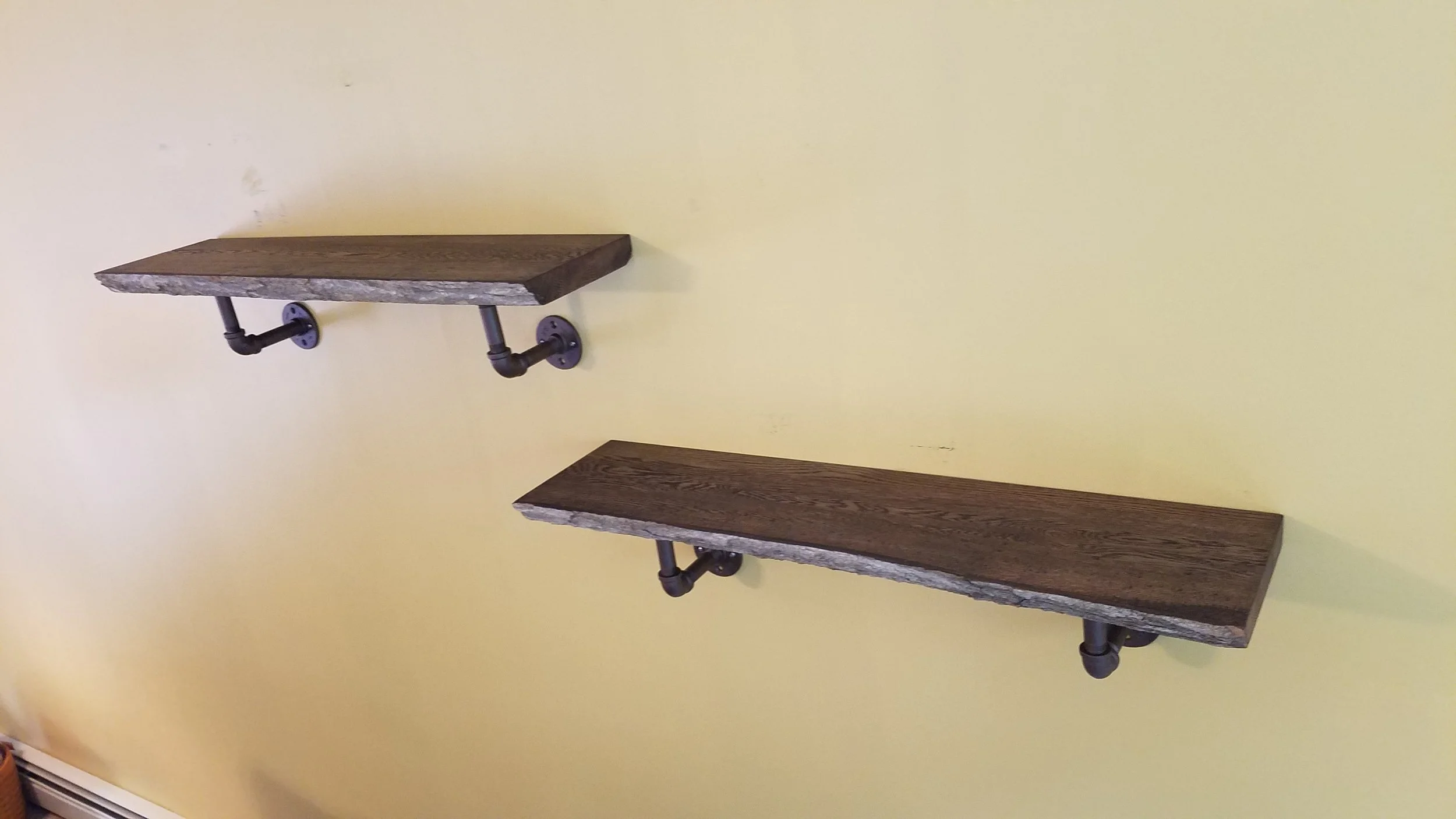 Two rustic wooden floating shelves mounted on a yellow wall with black pipe brackets.
