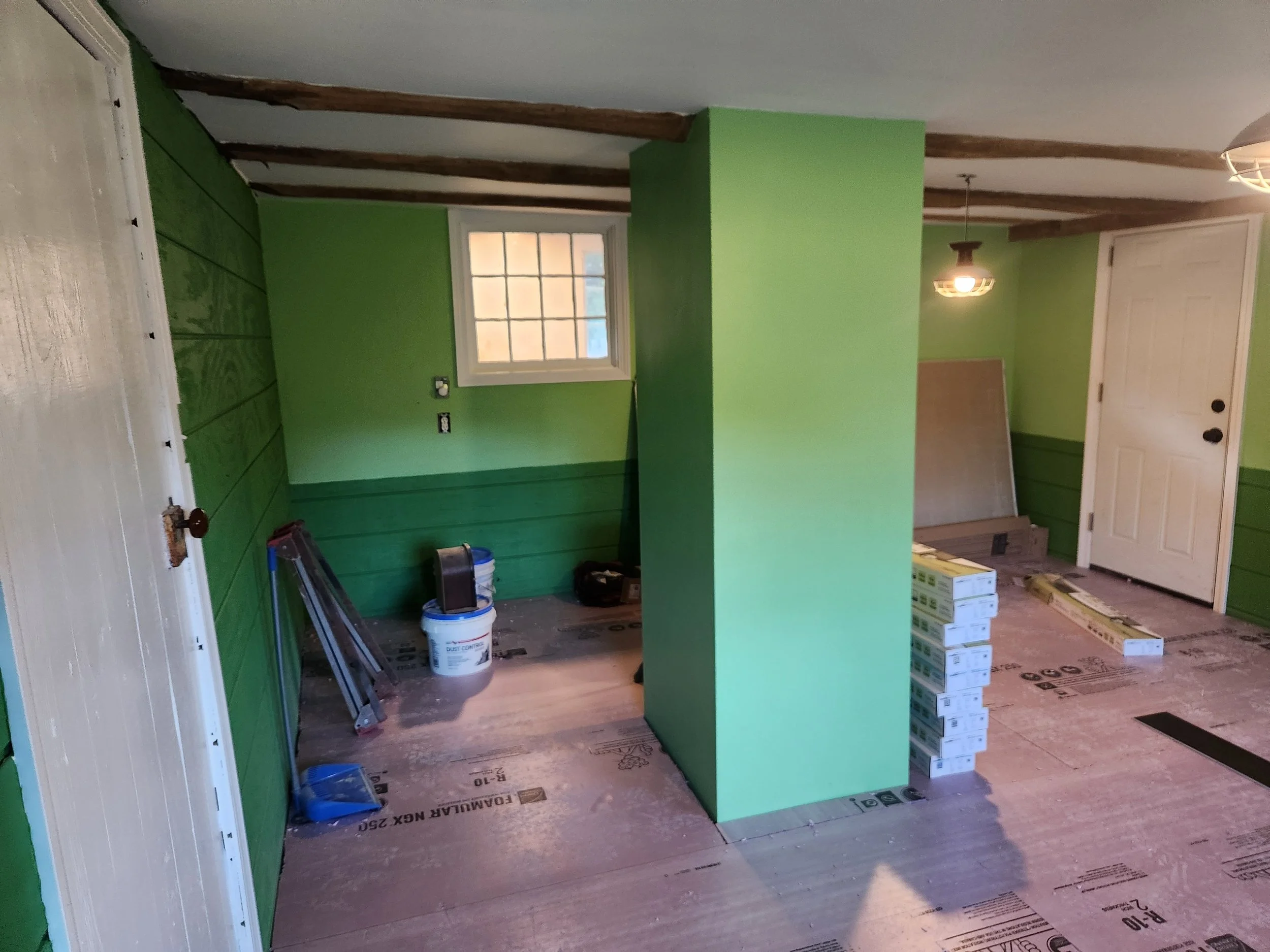 Room under renovation with green walls, ladder, buckets, and building materials on the floor.