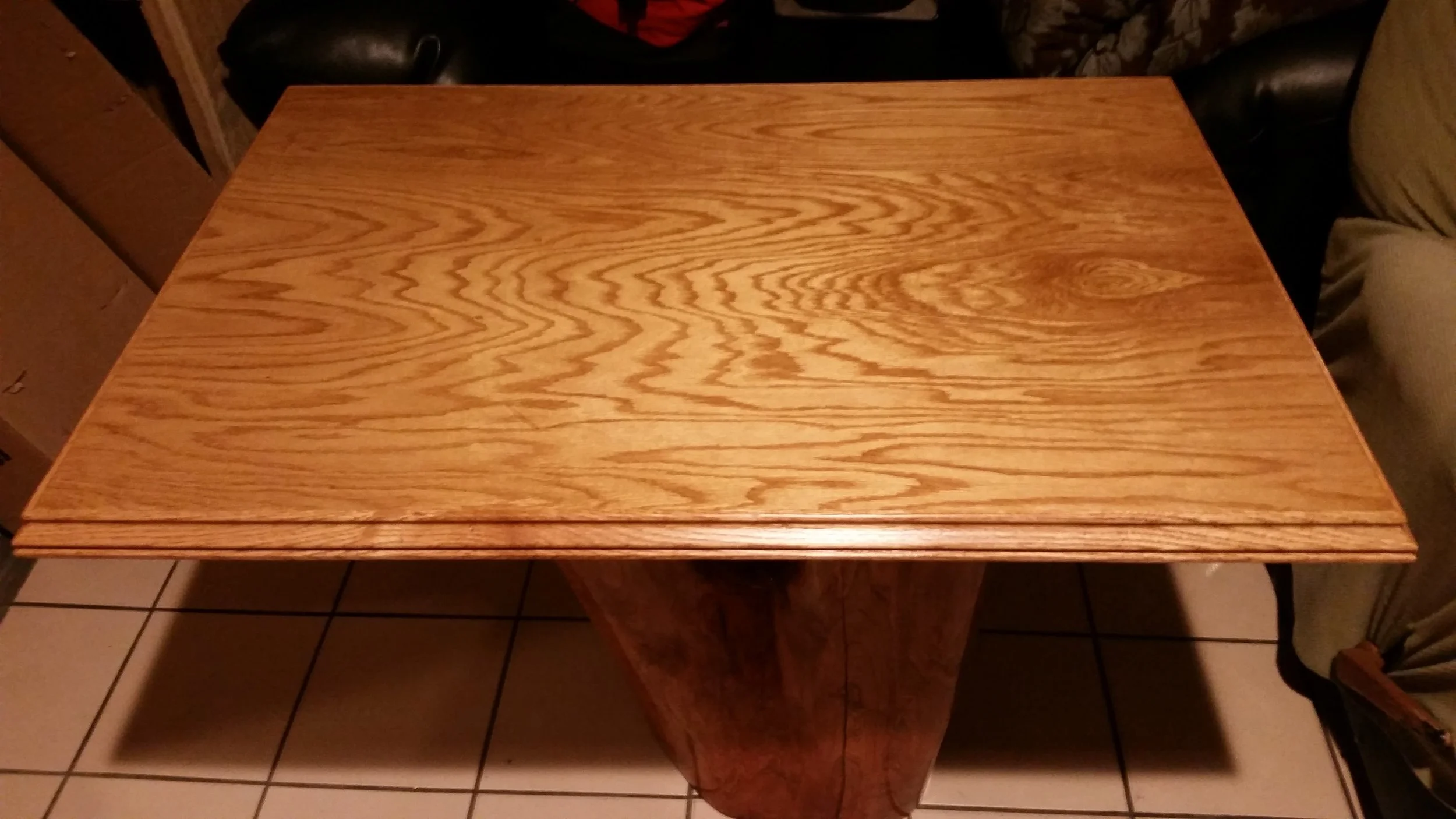 A wooden table with a rectangular top and curved base situated on a tiled floor, with black and beige chairs around it.
