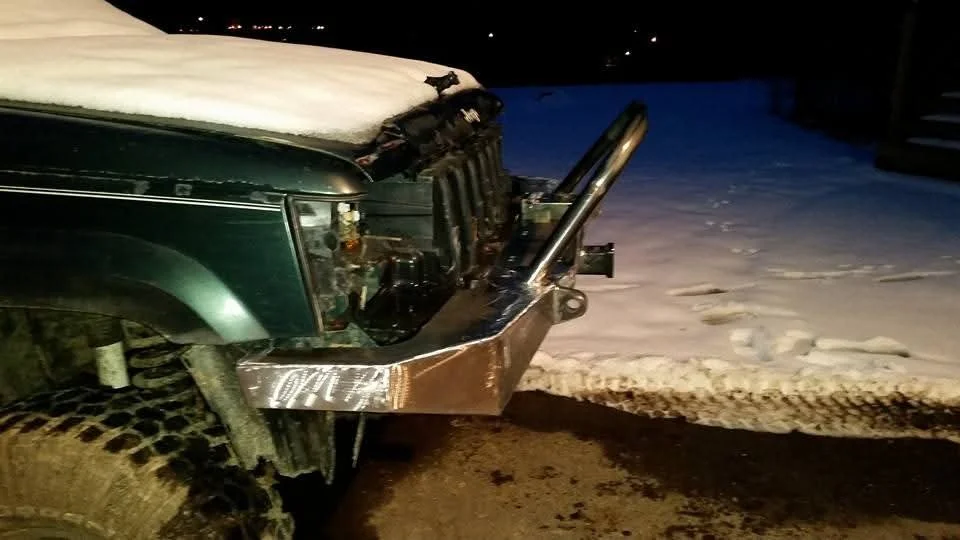 Front of a green vehicle with significant front-end damage, sitting on a snowy road at night.