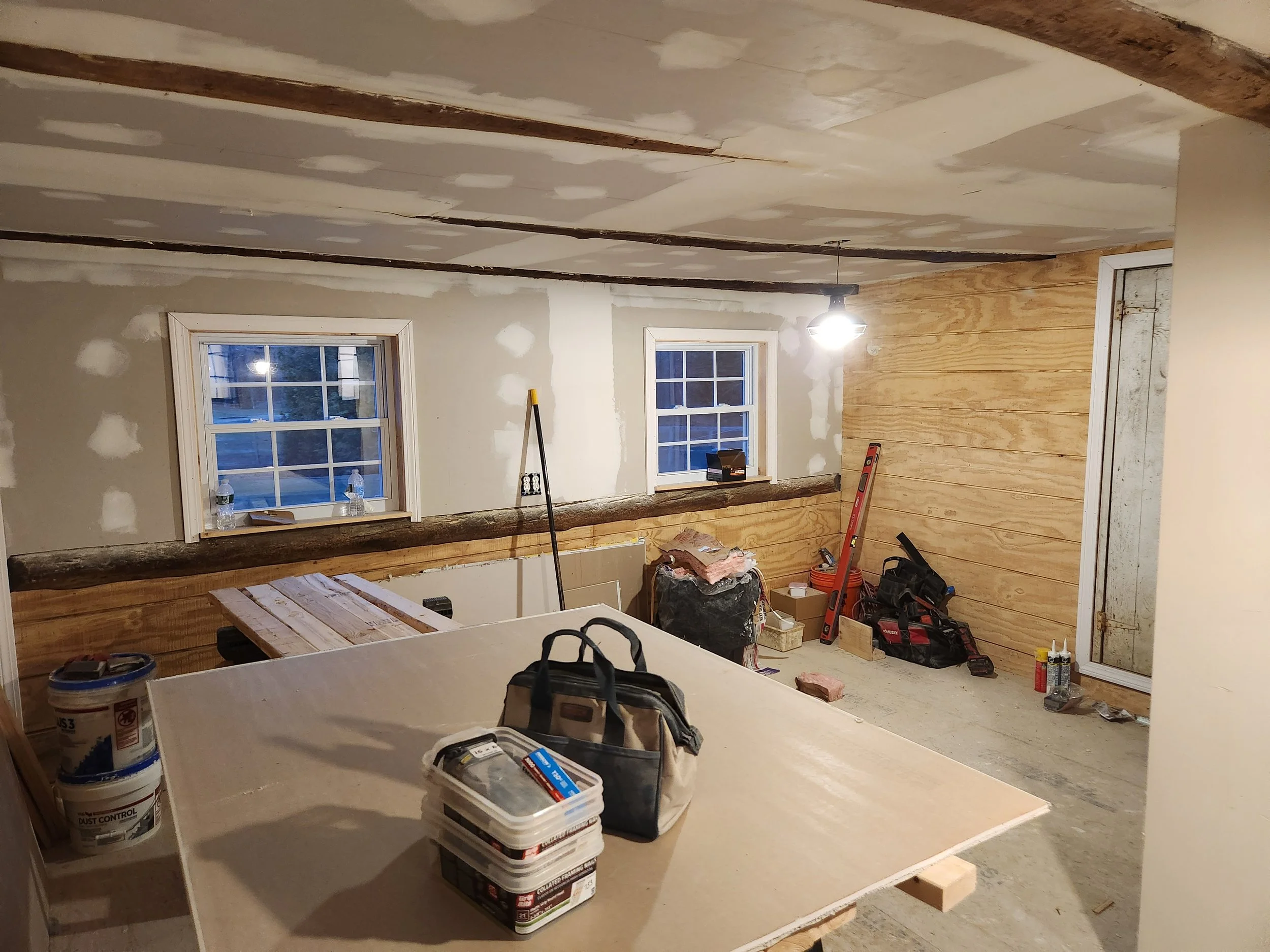 Room under construction with two windows, unfinished walls, tools, and materials.