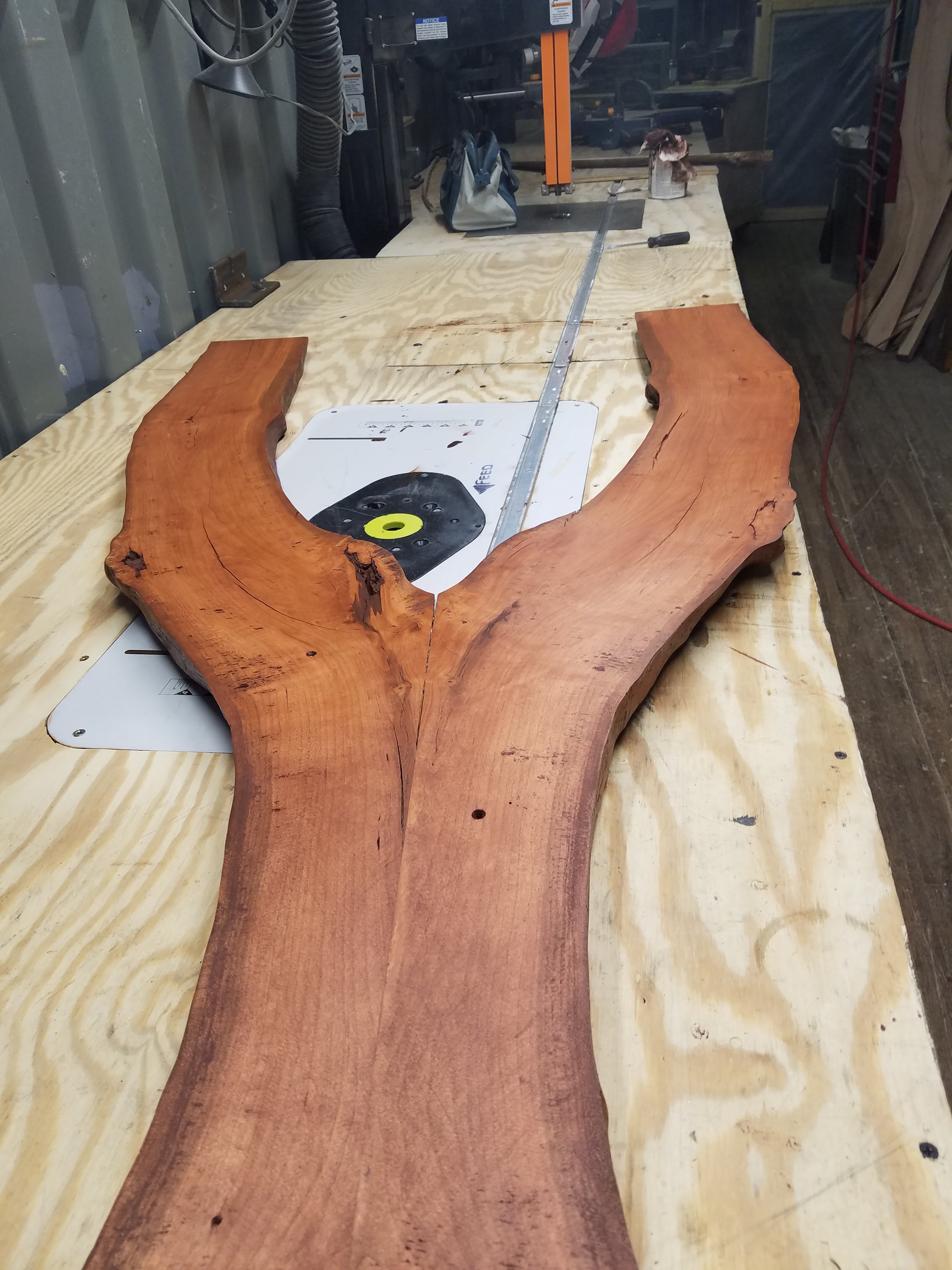 A large piece of polished wood with natural edges on a workbench, with tools and wood in a workshop.