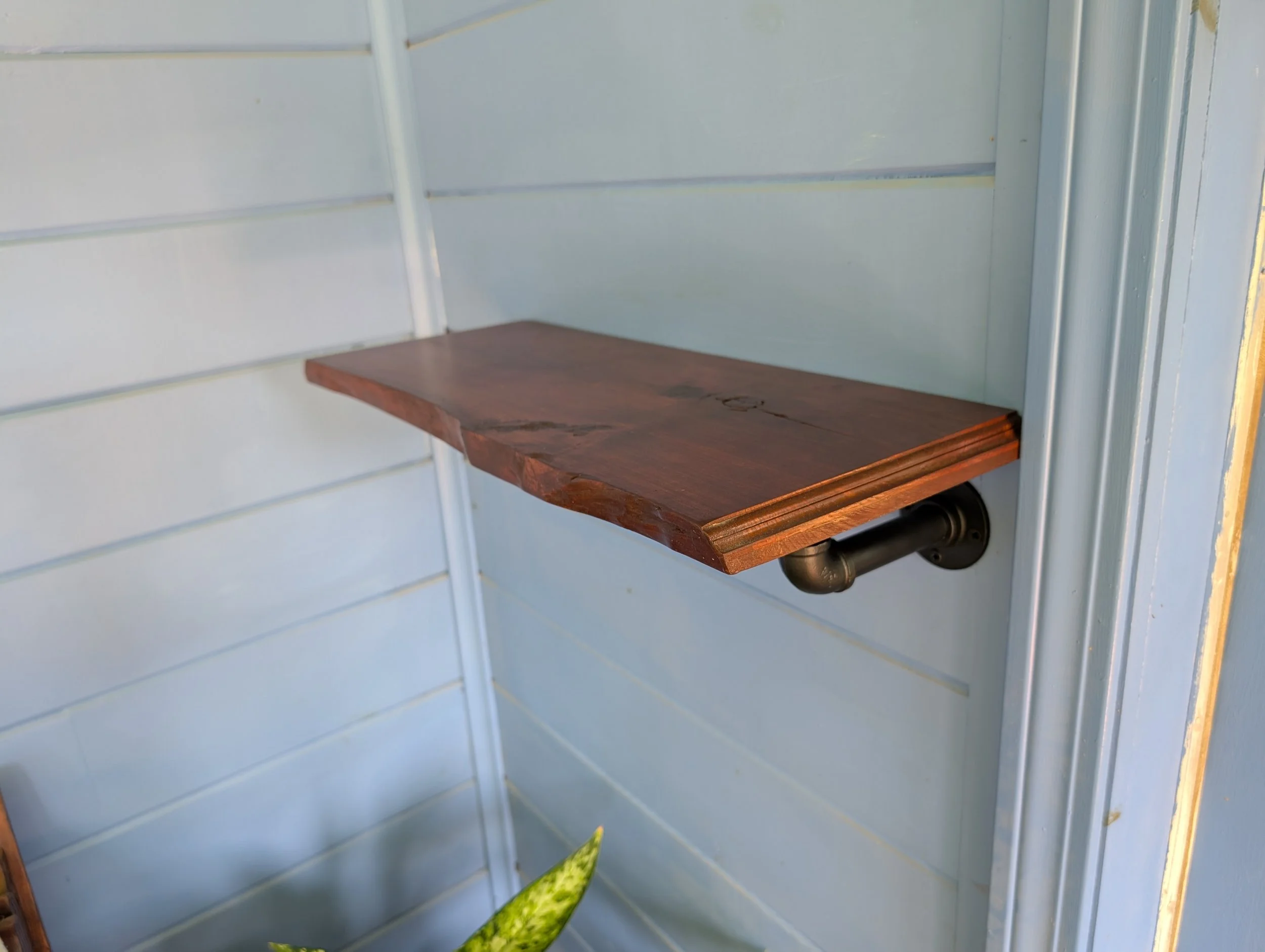 A wooden shelf attached to a light blue wall with metal pipes.