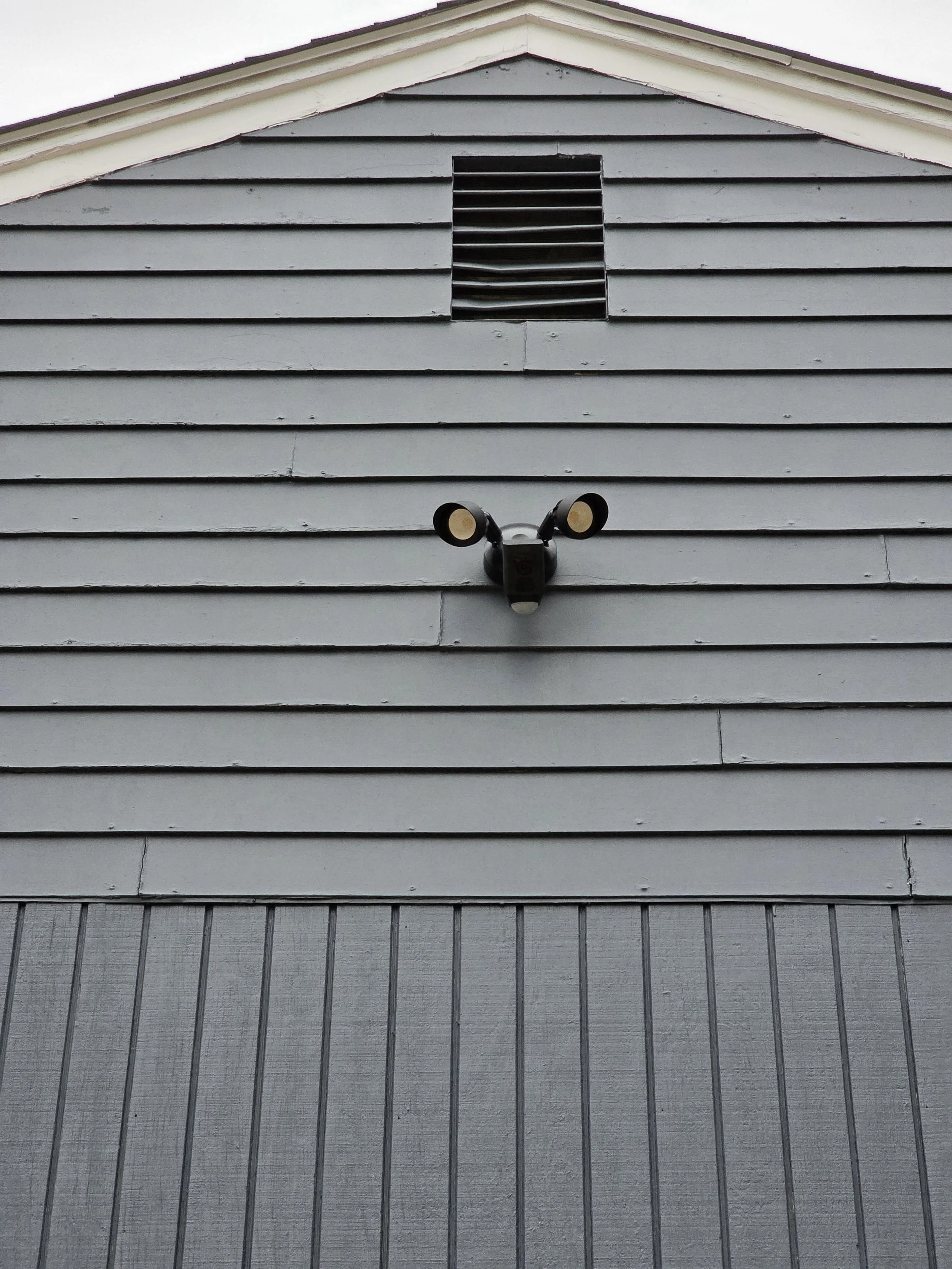 Exterior of a blue house with horizontal siding, a small vent near the roof peak, and a black security camera mounted on the wall.