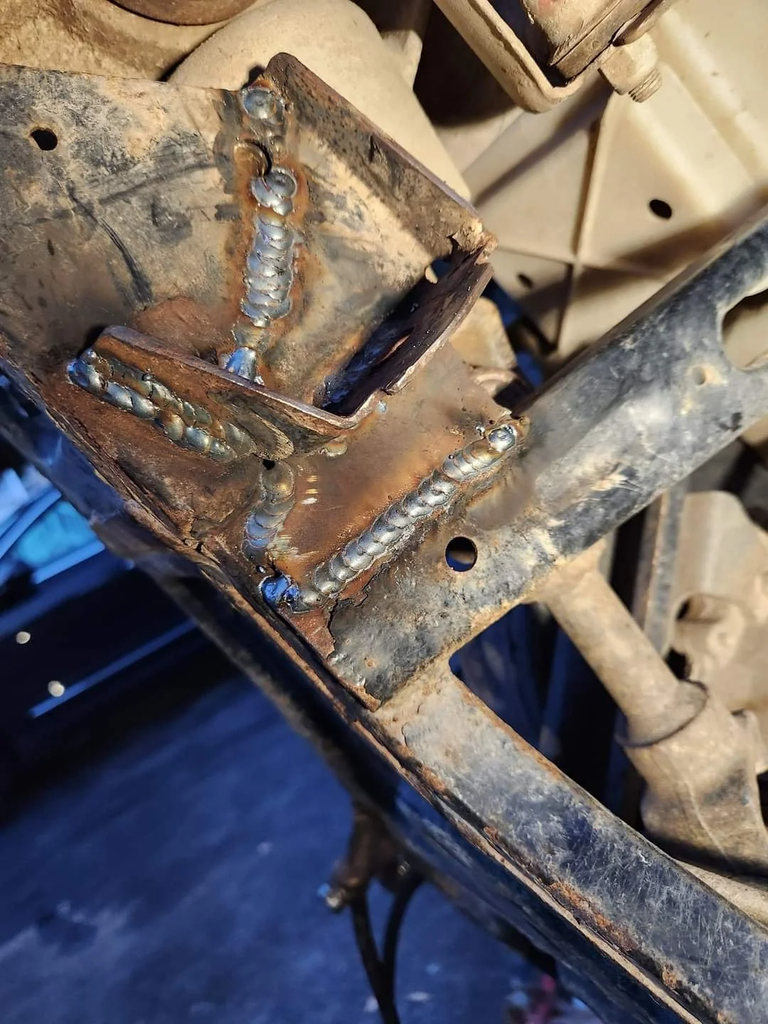 Close-up of a metal frame with freshly welded metal plates and joints, showing signs of rust and dirt.