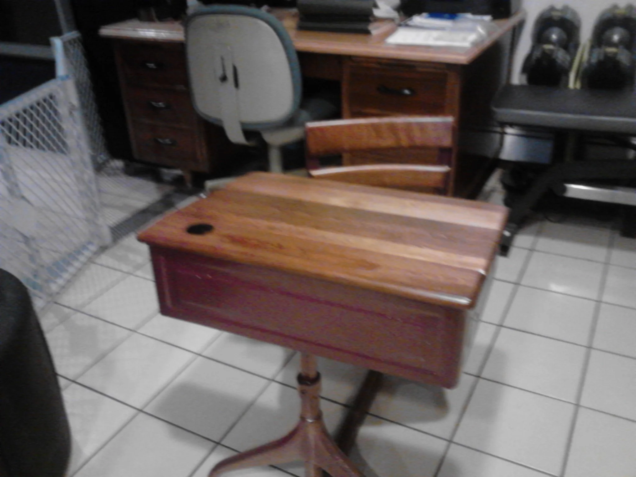 A small wooden table with a single drawer and a slightly curved top, situated on a tiled floor in a room filled with various furniture and equipment.