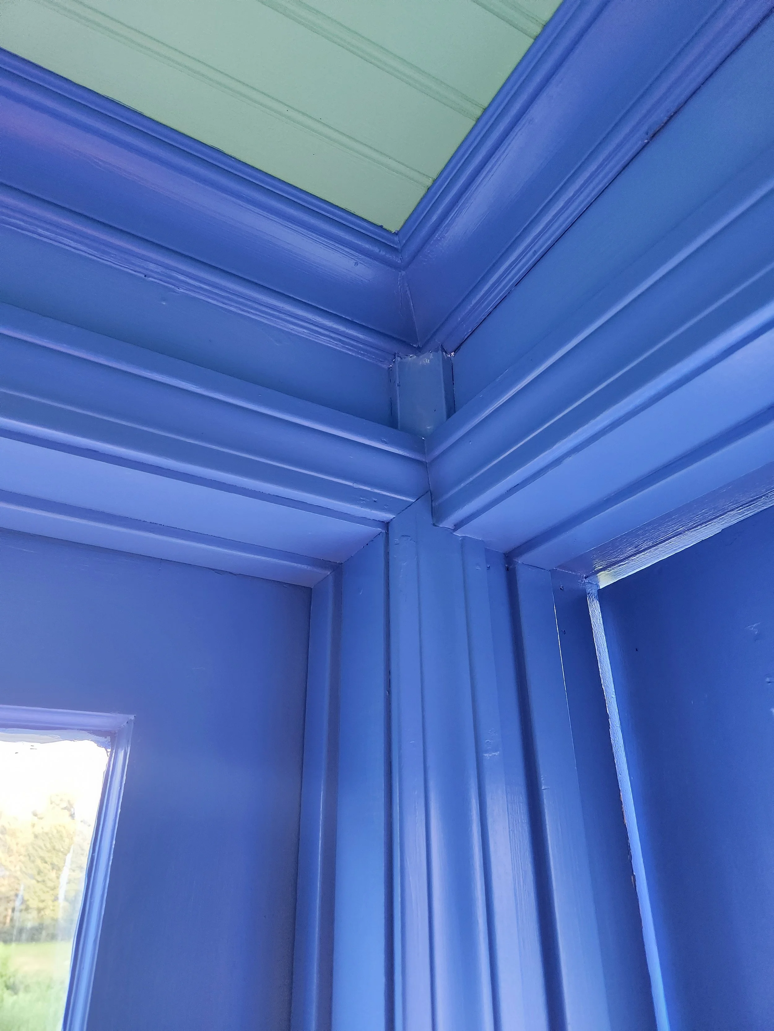 Close-up of blue painted window and door frame molding with crown molding at the corner of the ceiling.
