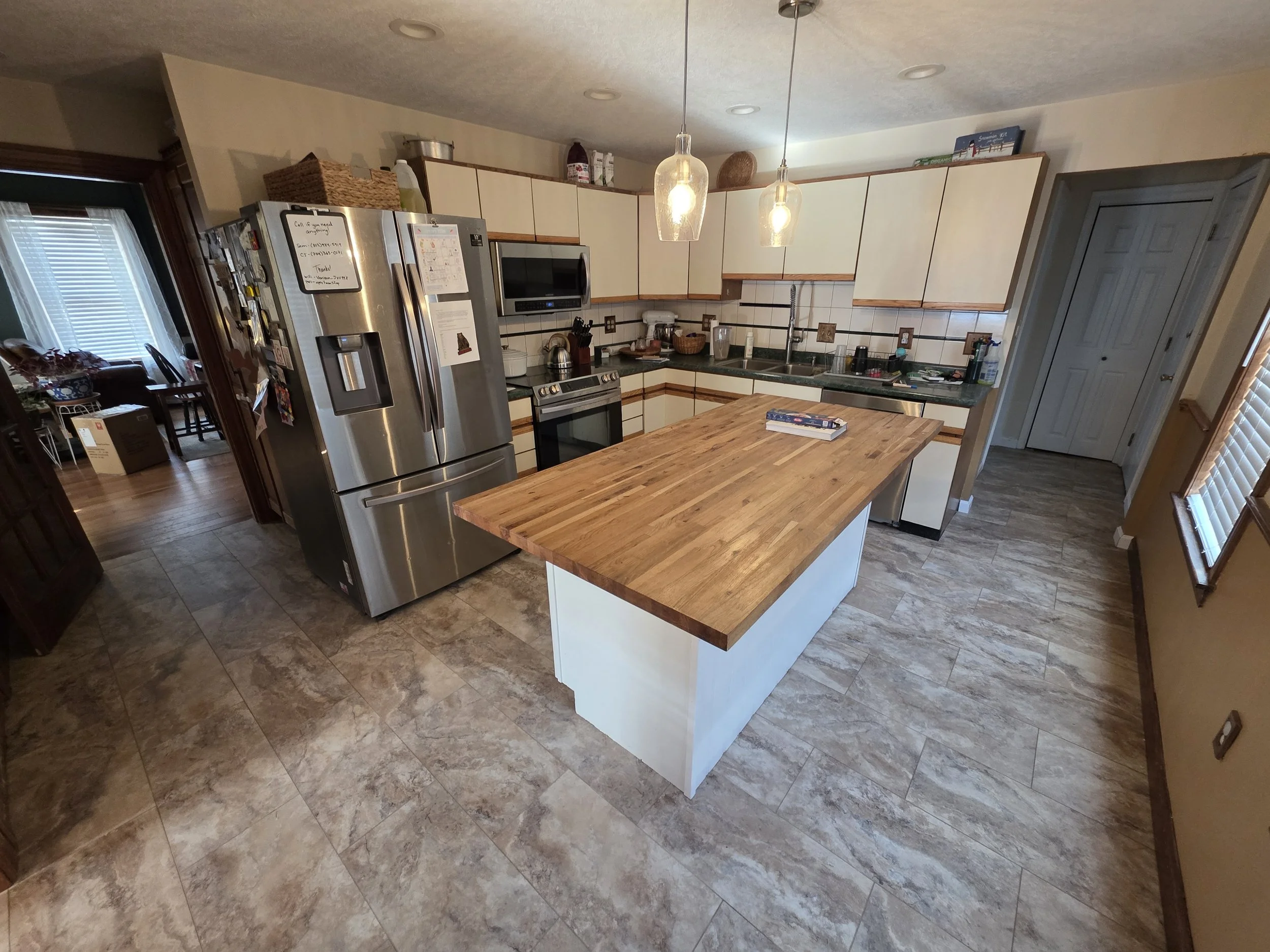 A kitchen with beige cabinets, a stainless steel refrigerator, a microwave, a stove, a double sink, and a wooden kitchen island.