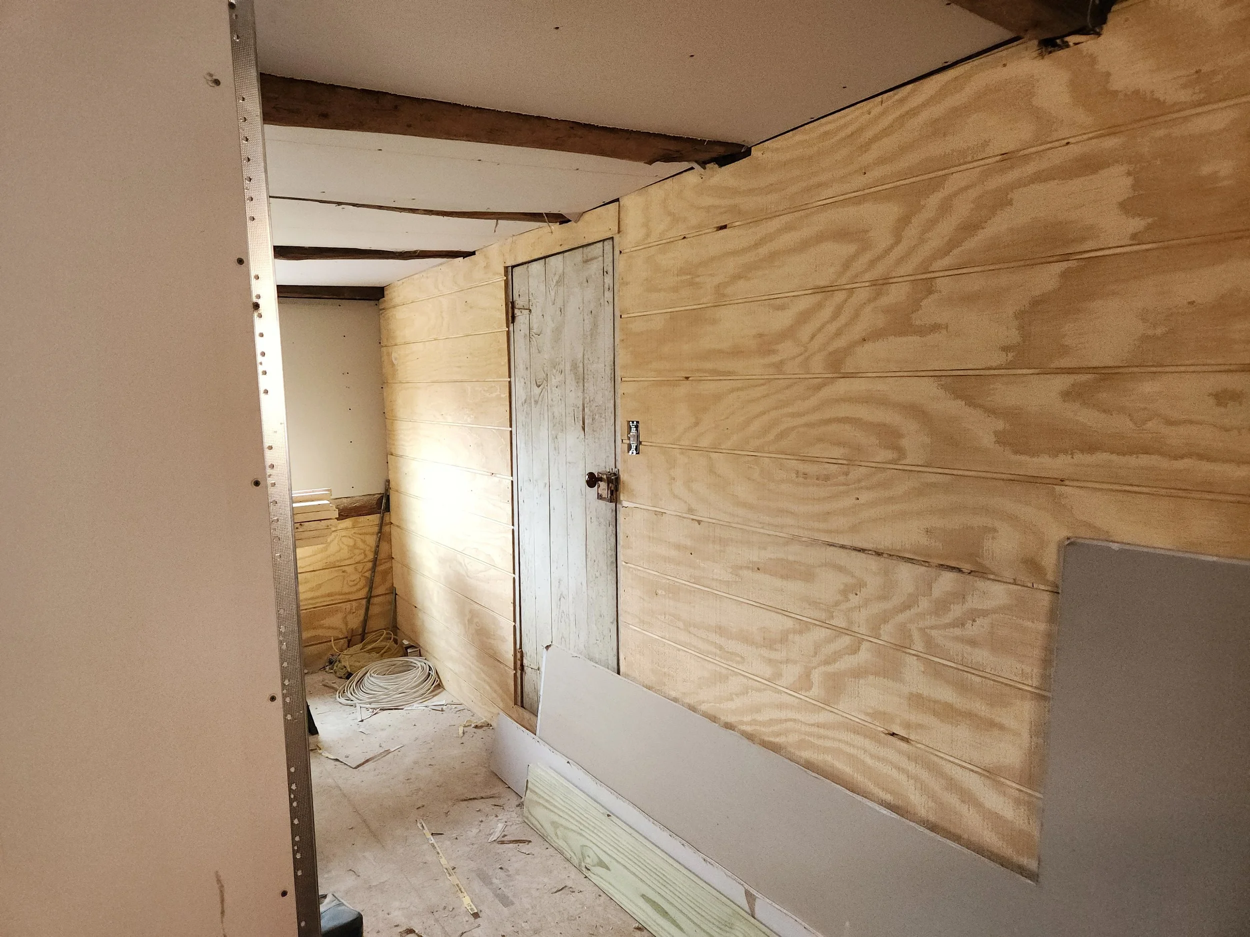 Interior of a construction site with unfinished walls. Wooden paneling on one wall, partially installed drywall on the other, construction tools, and materials on the floor.