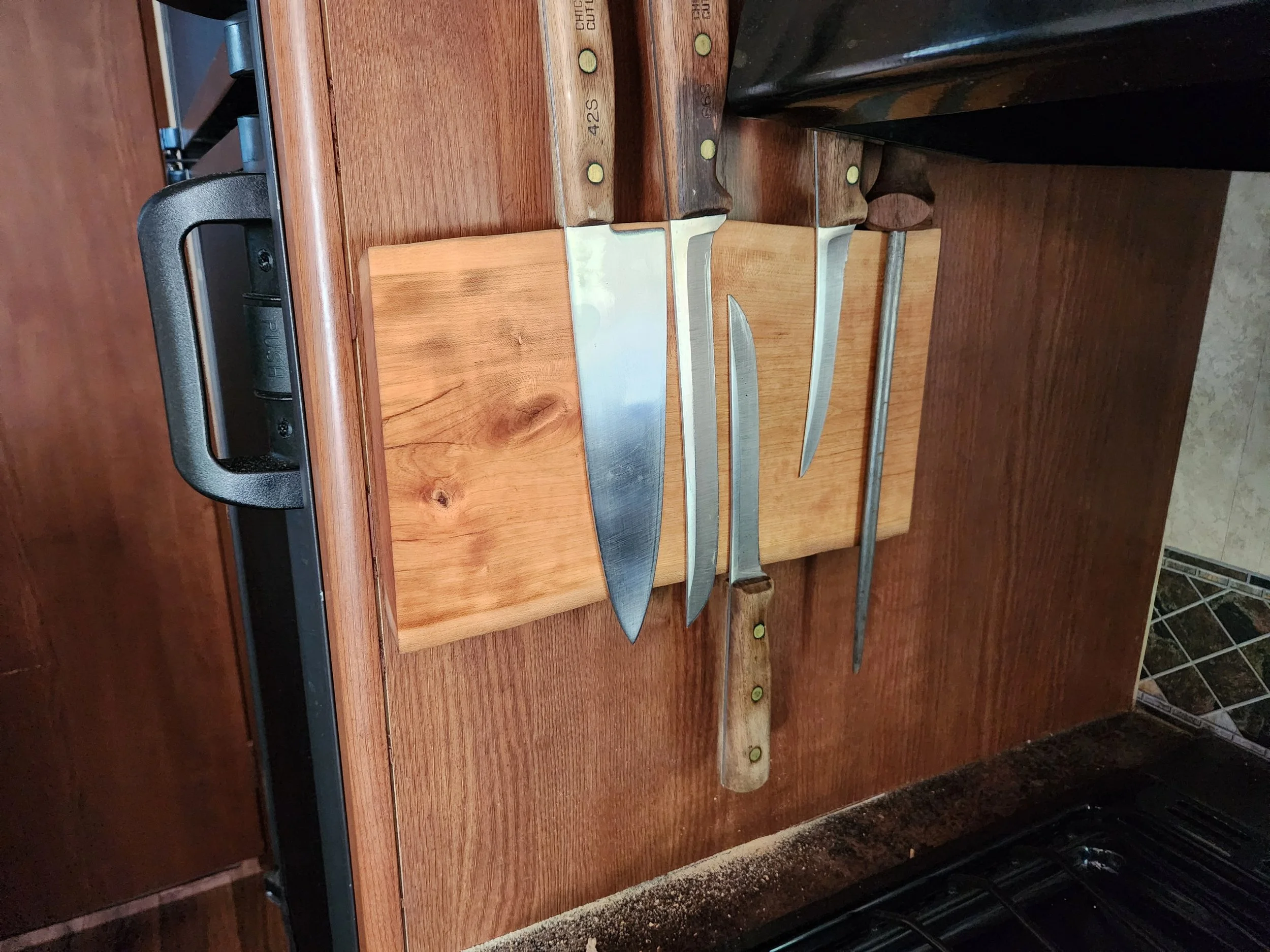 A wooden cutting board and four knives with wooden handles and stainless steel blades placed on a kitchen countertop.