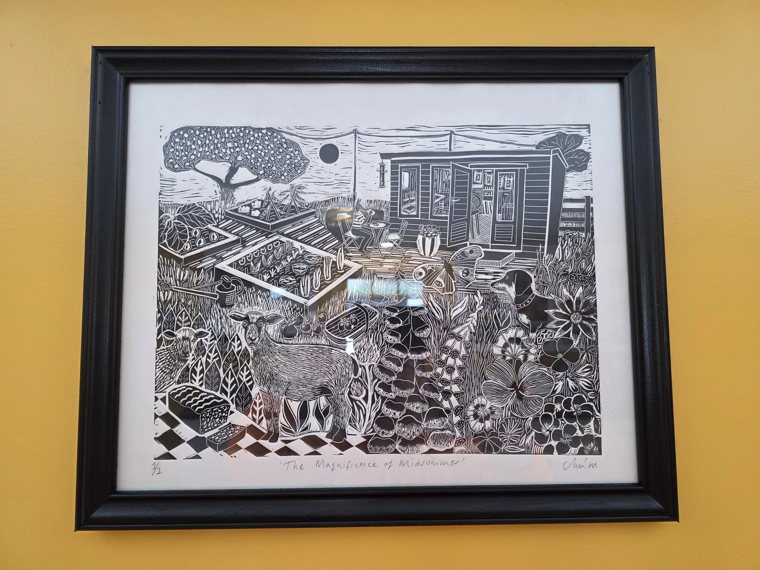 A framed black and white line drawing titled 'The Magnificence of Midomorna,' depicting a garden scene with a shed, chickens, vegetables, flowers, trees, a person sitting at a table, a dog, and various plants.