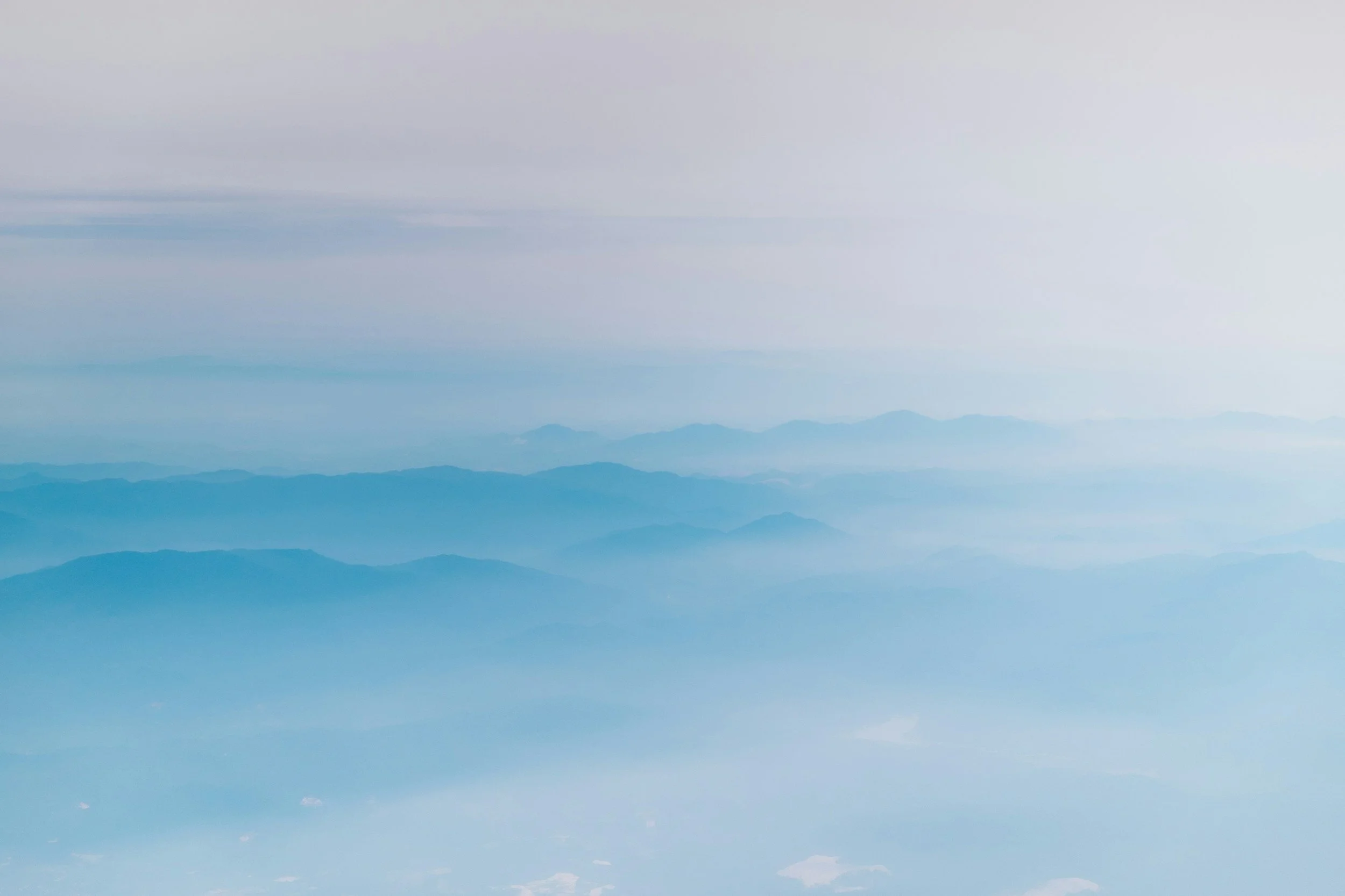 A mountain range with multiple layers of blue and gray mountains, viewed from above in a hazy or misty atmosphere.