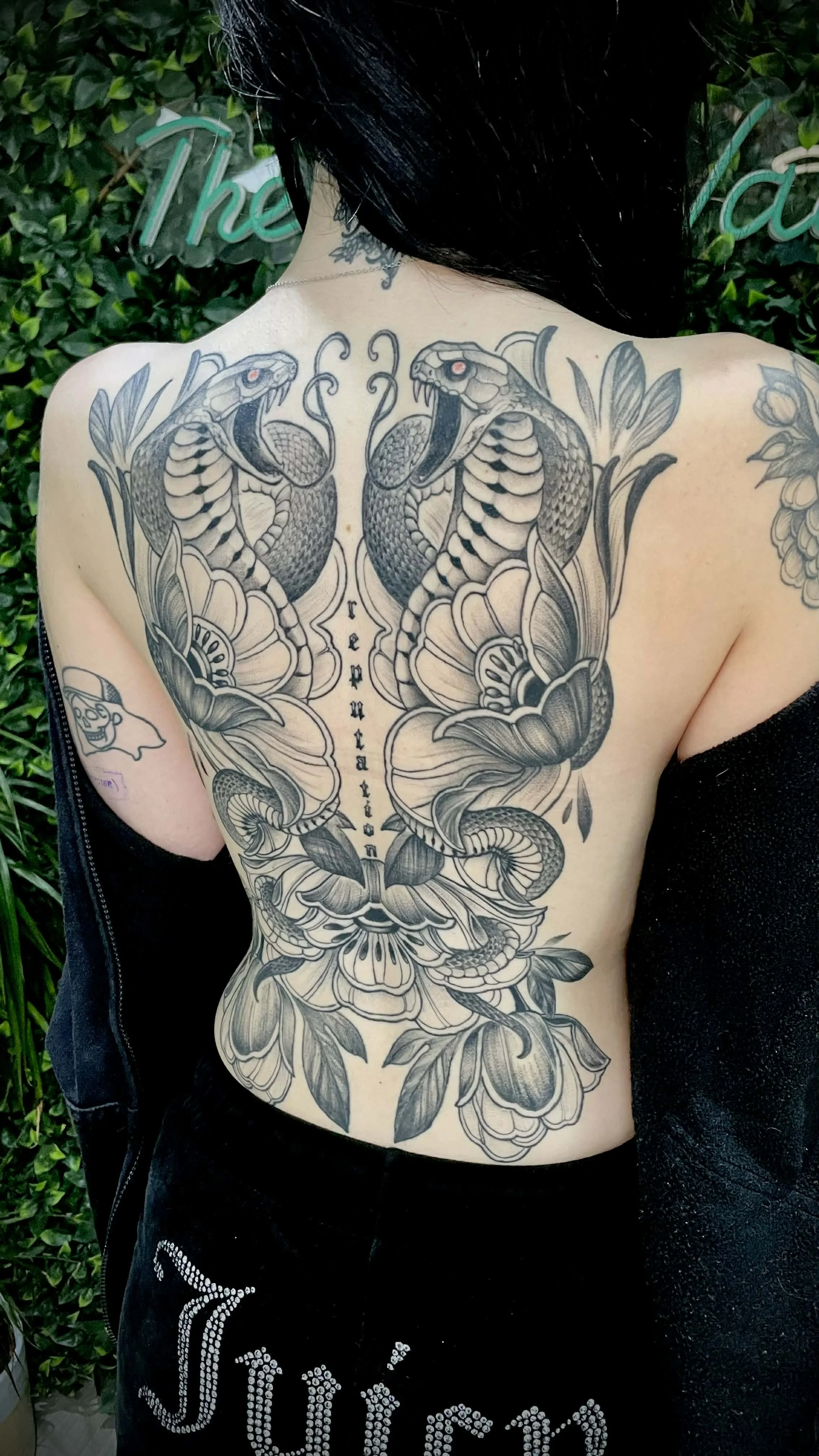 Back tattoo featuring two snakes, large flowers, and the word 'reputation’ in vertical script. Taylor swift 