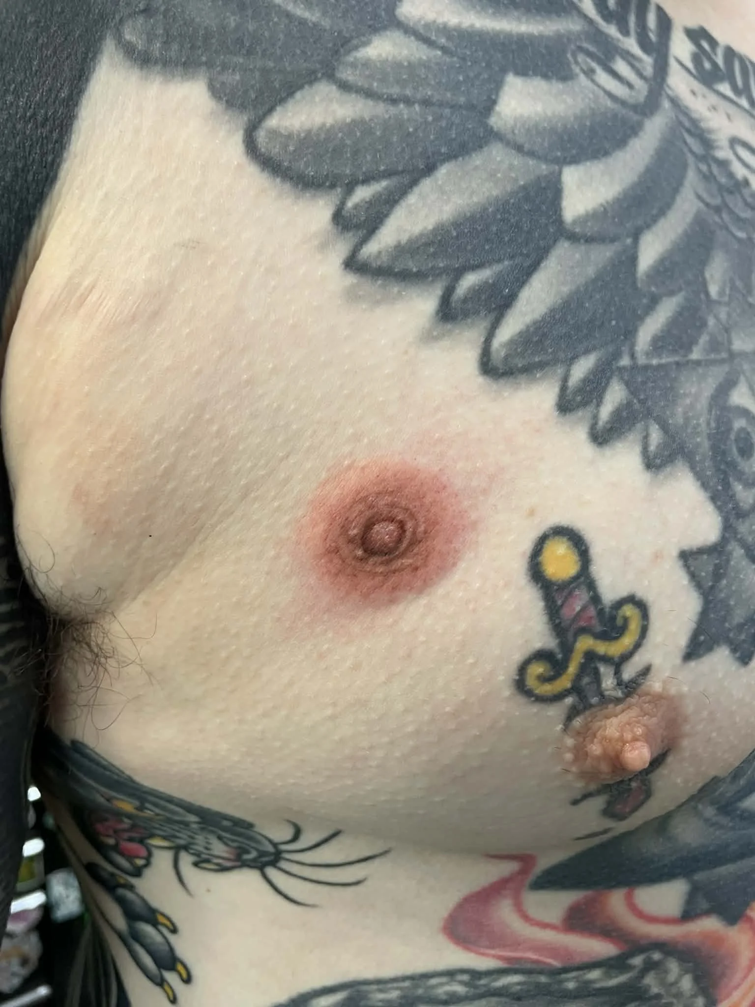 Close-up of a person's chest with tattoos, including a dagger and floral designs, and a nipple.