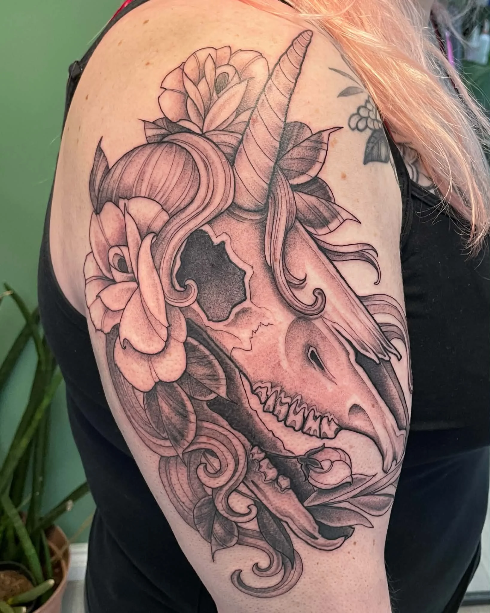 Black outline tattoo of a detailed skull with floral and succulents on person's upper arm.