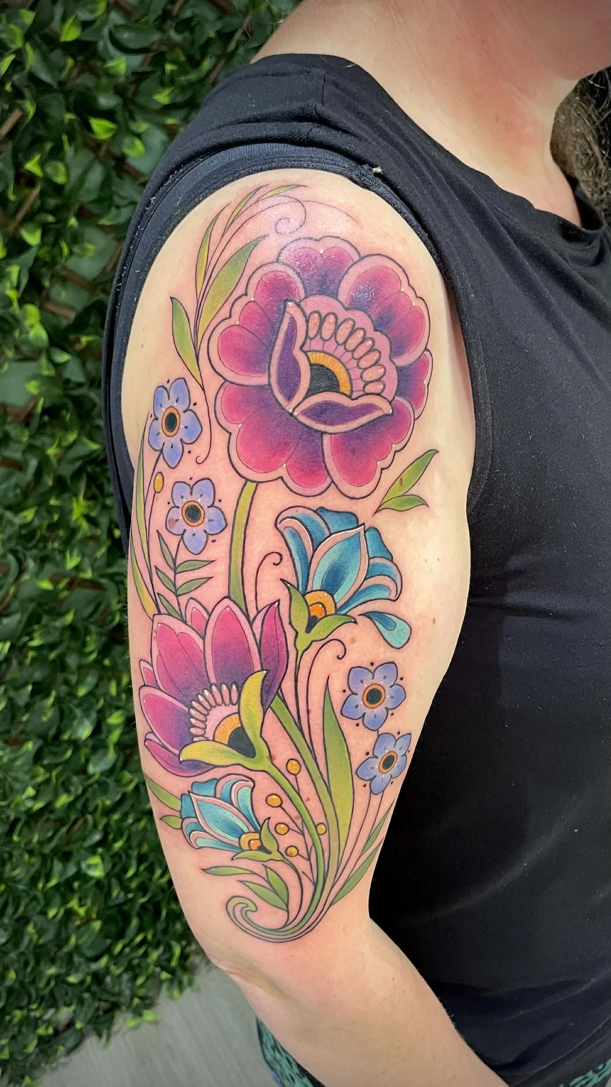 Colorful floral tattoo on upper arm, featuring pink, purple, and blue flowers with green leaves.