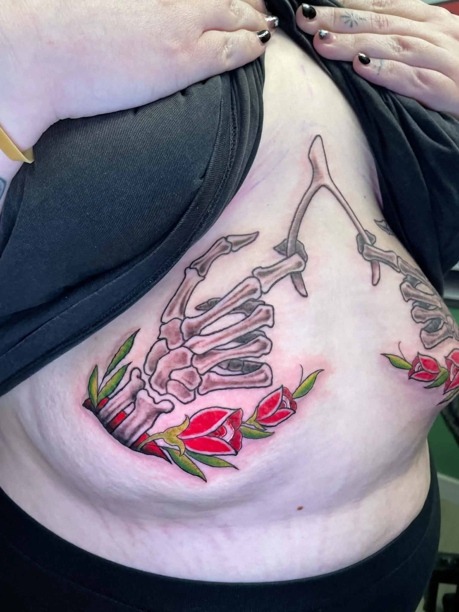 Close-up of a person's side abdomen showing a tattoo of a large skeleton key with roses and leaves. The person is wearing a black shirt unzipped to reveal the tattoo.