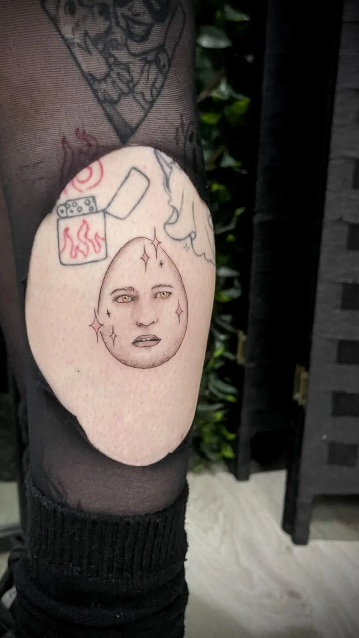 Tattoo of a face with a moon shape, with stars and facial features, on a person's arm. Surrounding tattoos include a lighter, a cigarette, and a face in profile. Eggward twilight Edward Cullen 