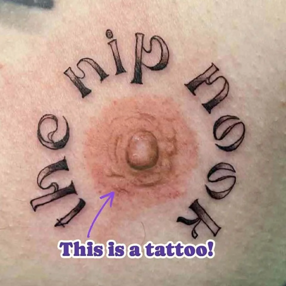 Close-up image of a tattoo that features the phrase 'love yourself' in a circular arrangement around a raised, flesh-colored bump or mole on skin with surrounding redness. The tattoo is upside down in the image, and a purple arrow points to the bump with text that reads 'This is a tattoo!'.