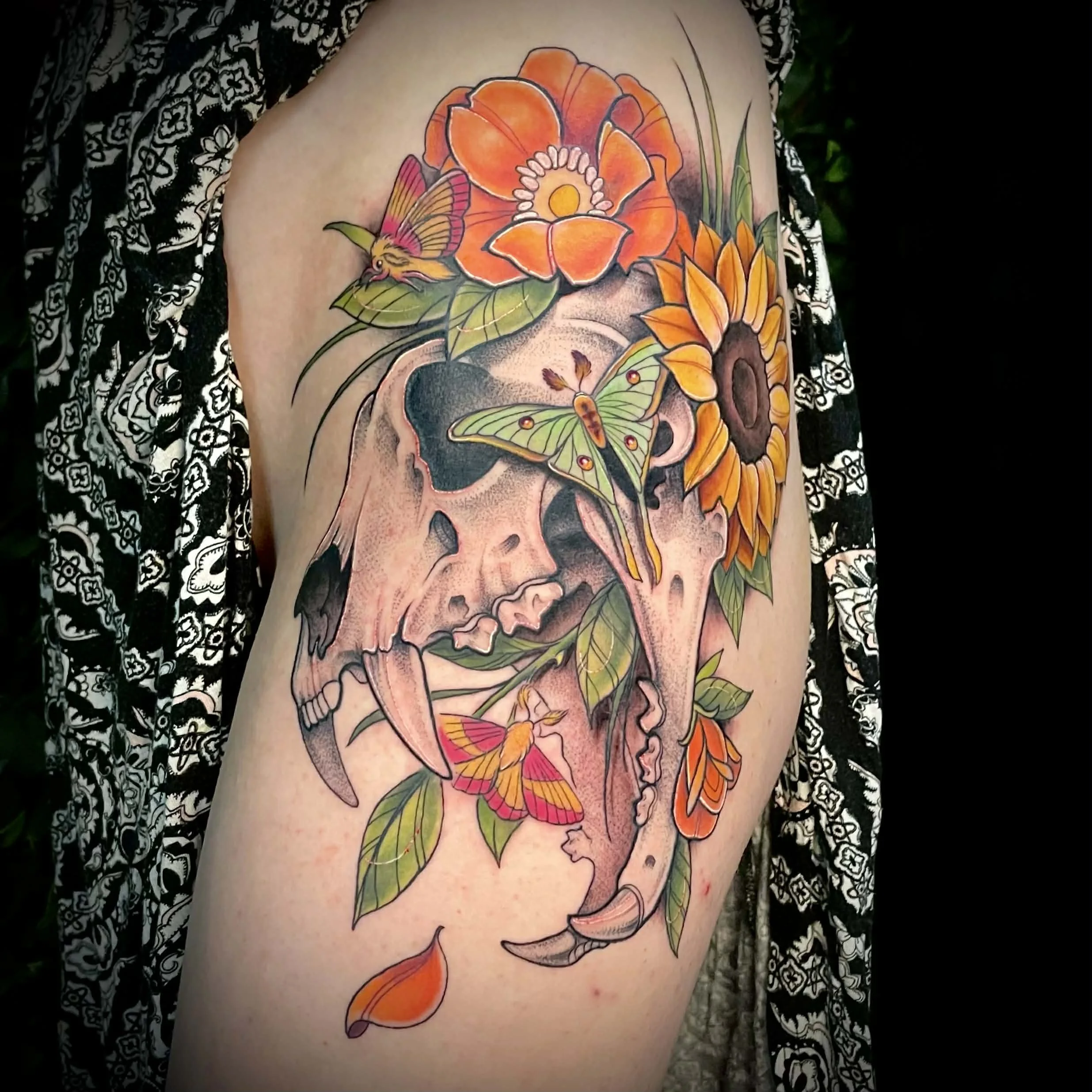Colorful tattoo of a skull surrounded by flowers, butterflies, and leaves on a person's arm.