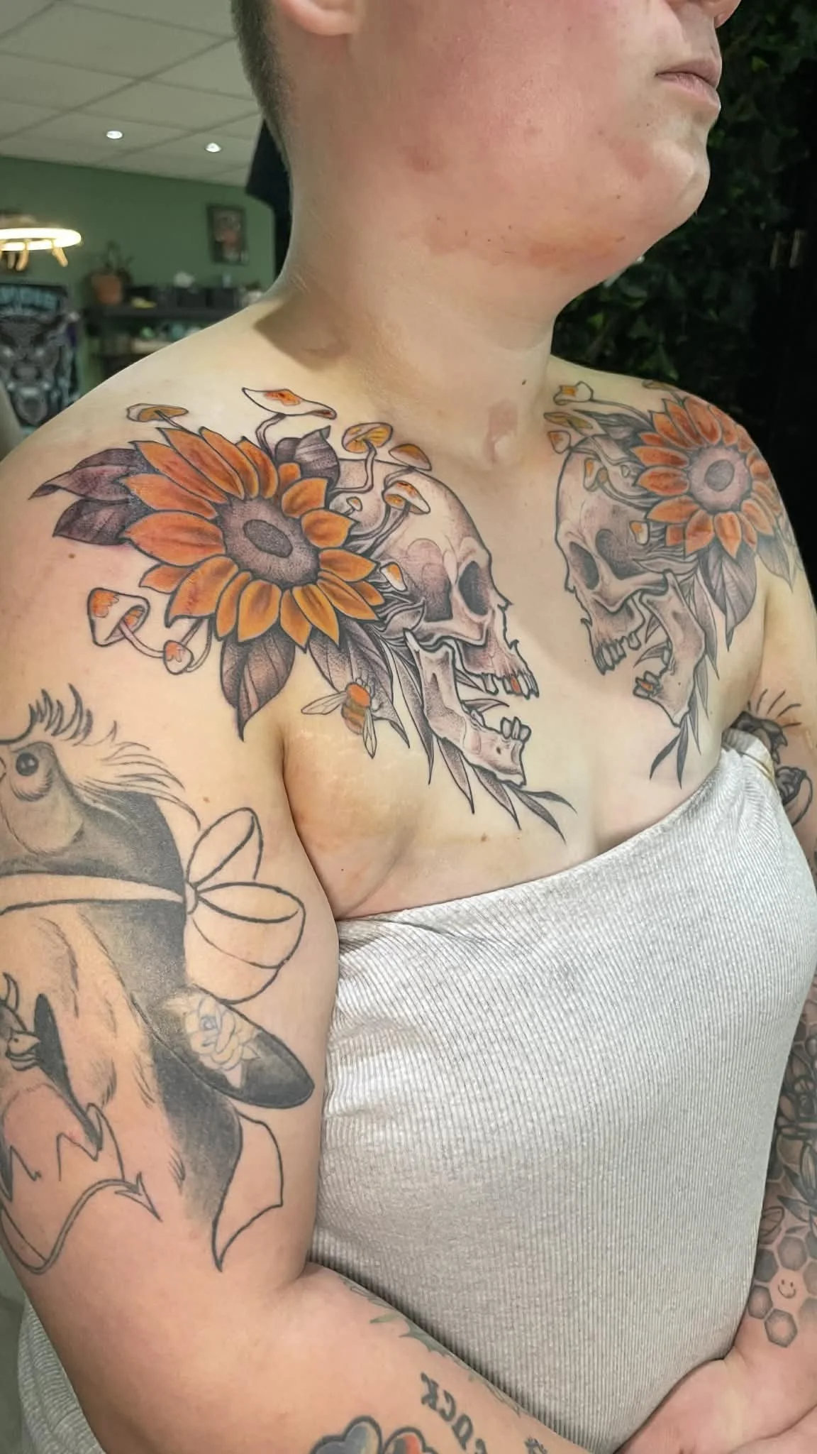 A person with tattoos of skulls and sunflowers on their chest, shoulders, and arms.