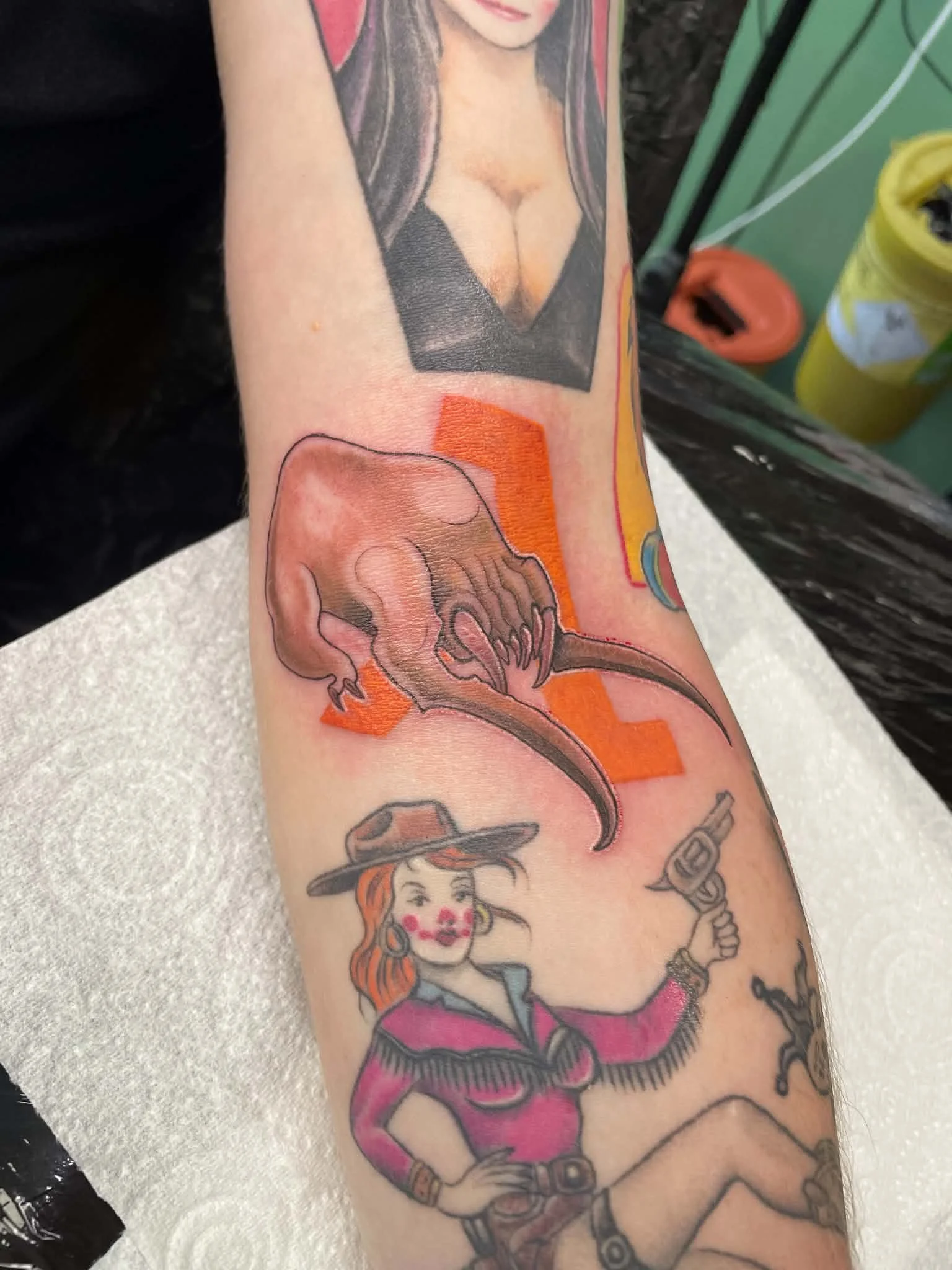 A colorful tattoo sleeve on a person's arm featuring various images including a woman's face, a skull with a fire, a small girl with a hat, and other decorative elements.