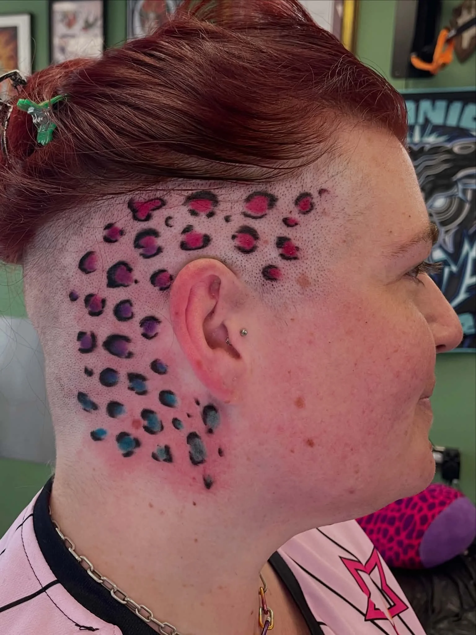 Side view of person's head with temporary leopard print hair tattoo in pink, black, and blue, and loose brown hair.