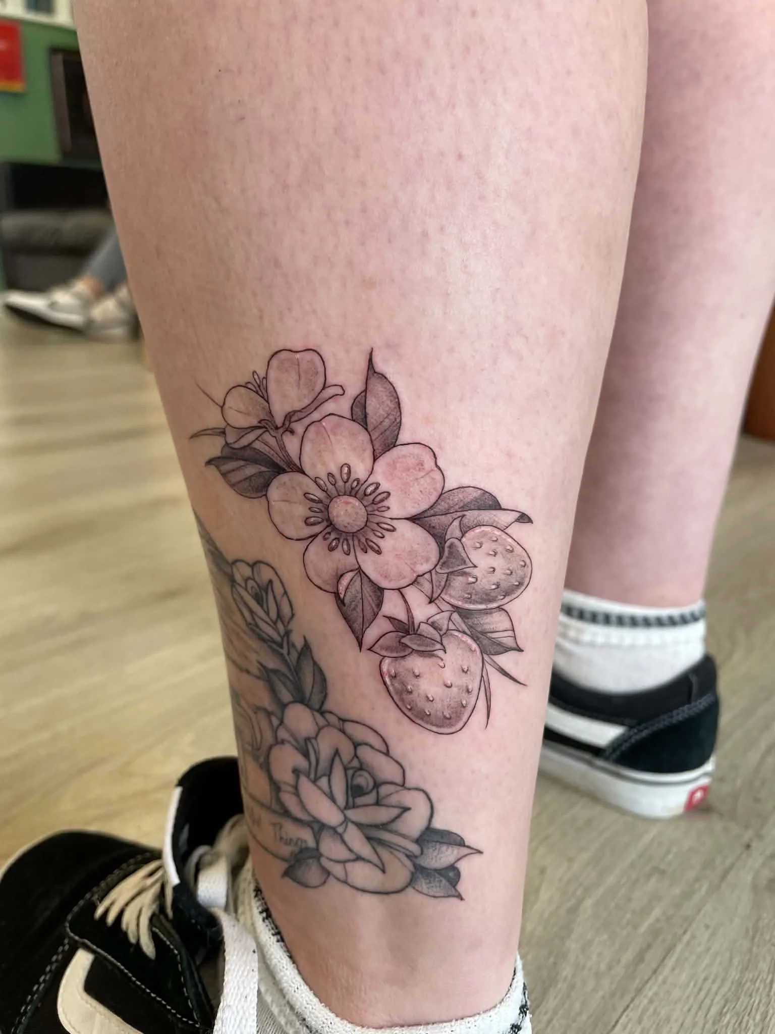 A person's leg with a black and white floral tattoo, including strawberries and various flower blossoms.