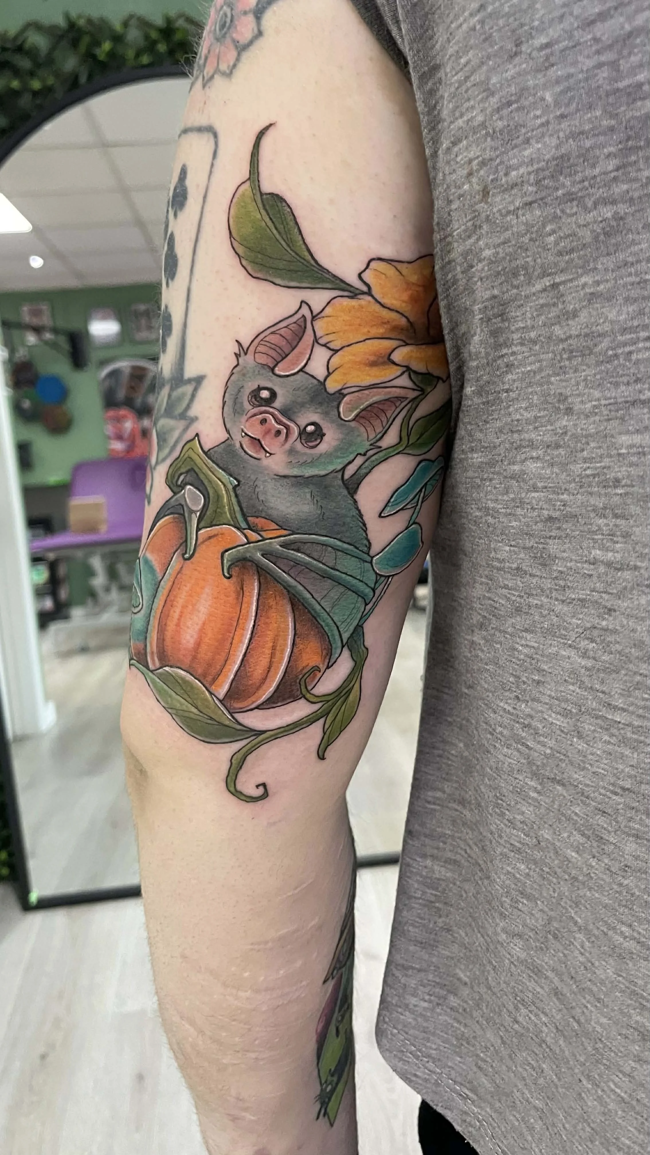 Tattoo of a bat with wings, sitting inside a pumpkin, surrounded by flowers and leaves.