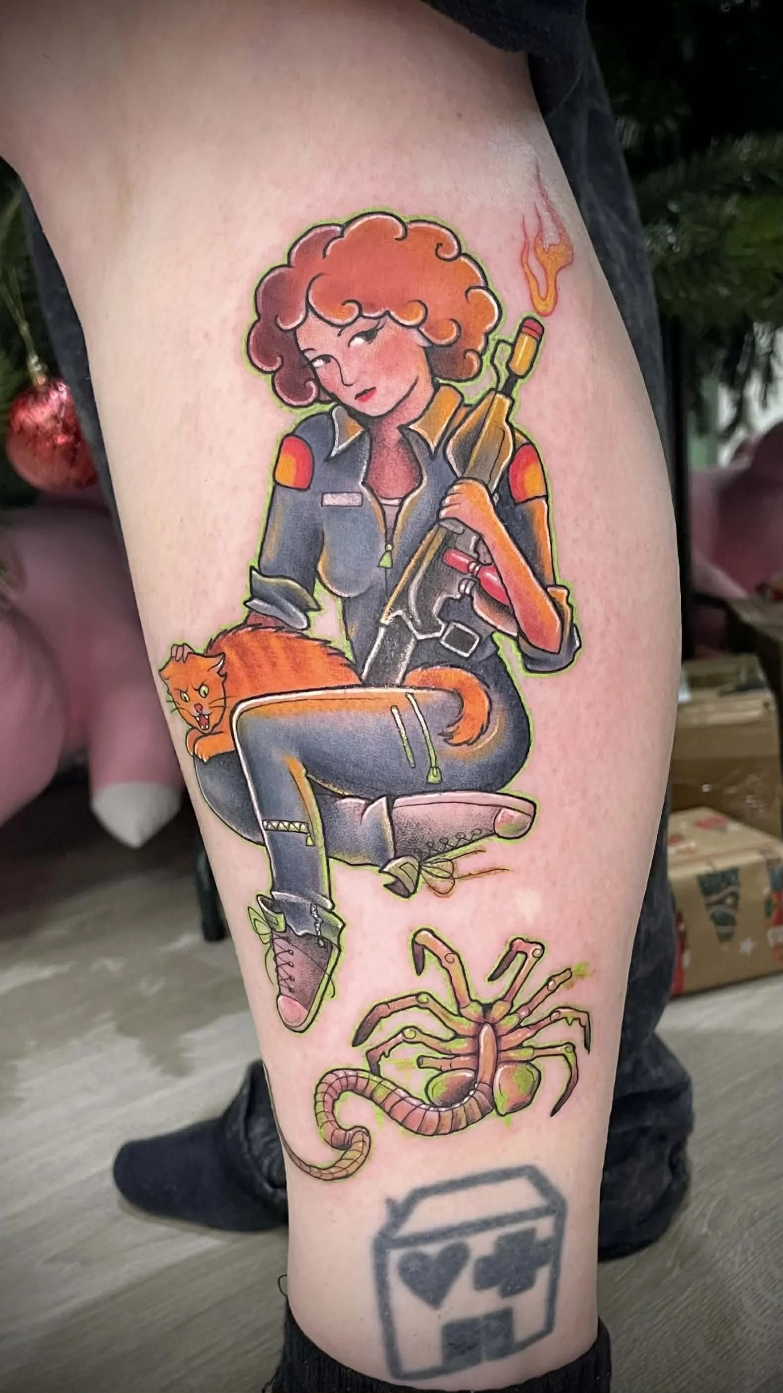 Colorful tattoo of a woman with curly hair in a military-style jacket holding a flame thrower, with a cat sitting on her lap and a cartoonish insect or creature below. Alien, Ellen ripley, jonesy alien movies, xenomorph 