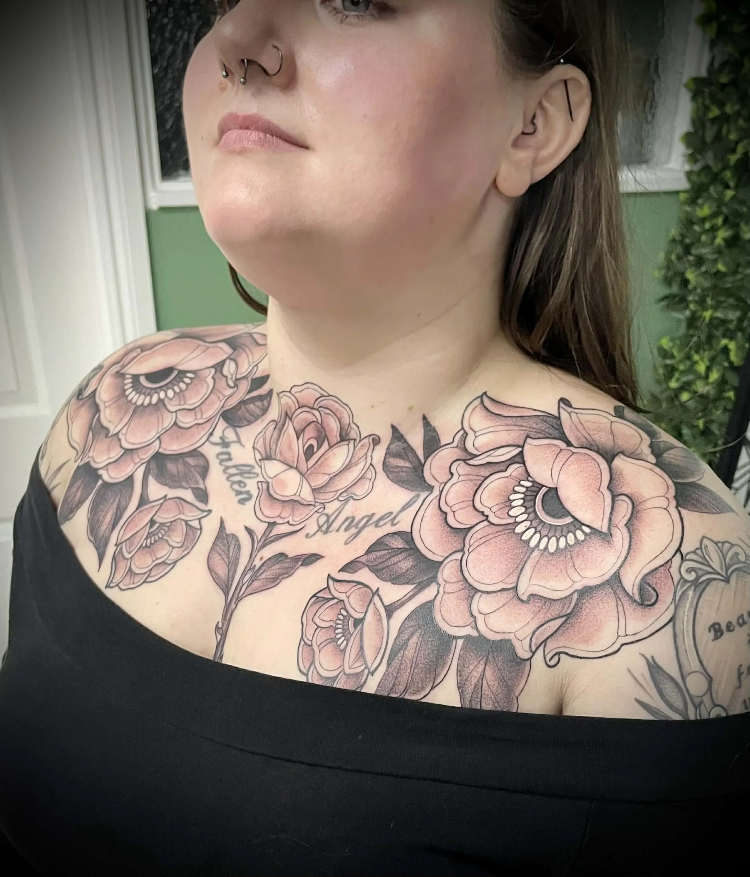 A woman with floral tattoos on her chest and shoulders, with the words 'Angel,' 'Faith,' and 'Beau' included in the ink, visible in a black off-shoulder top.