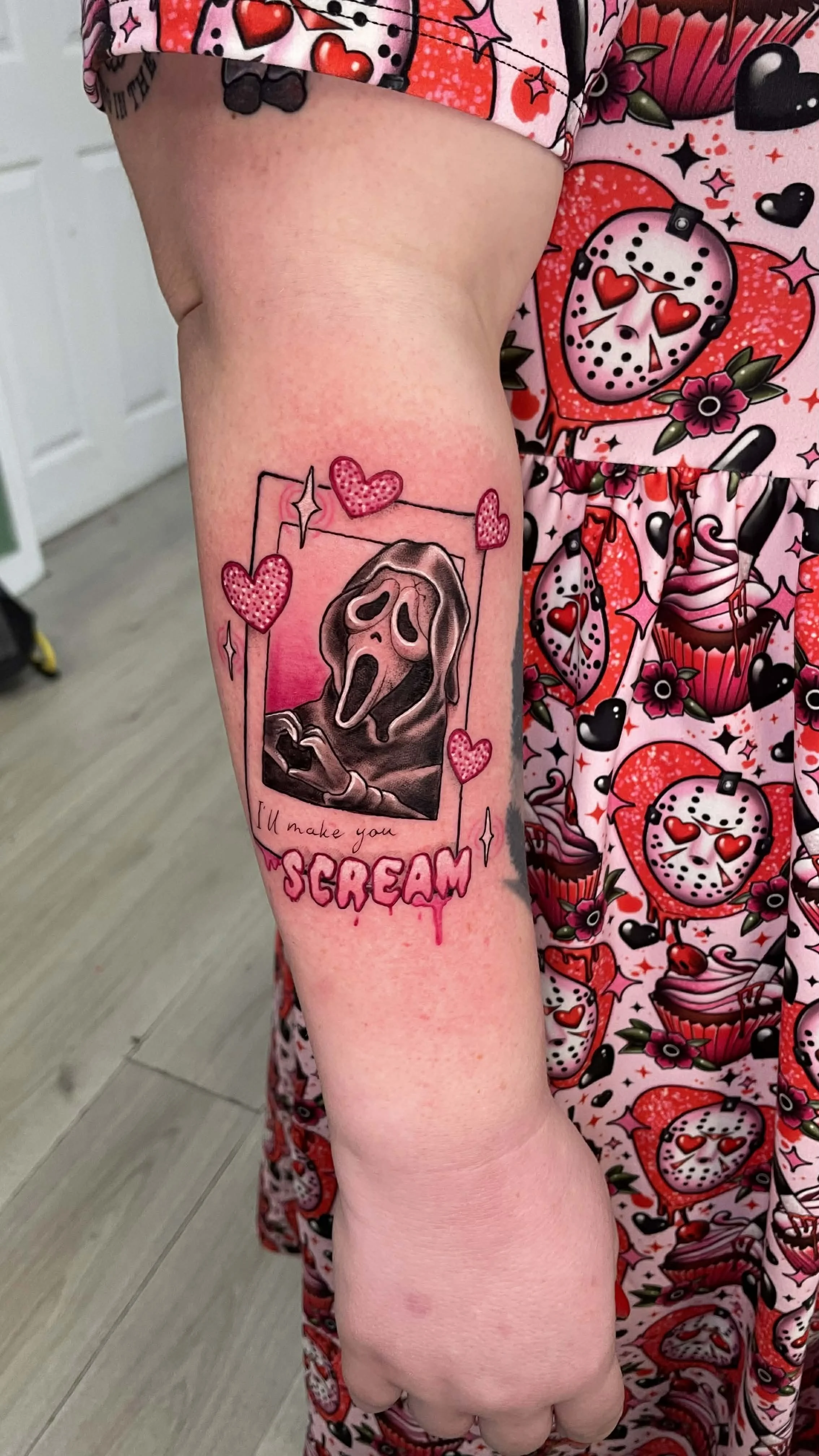Tattoo of the character Ghostface from the movie Scream, with the quote "I'll make you" and the word "SCREAM" in dripping pink paint, surrounded by pink hearts.