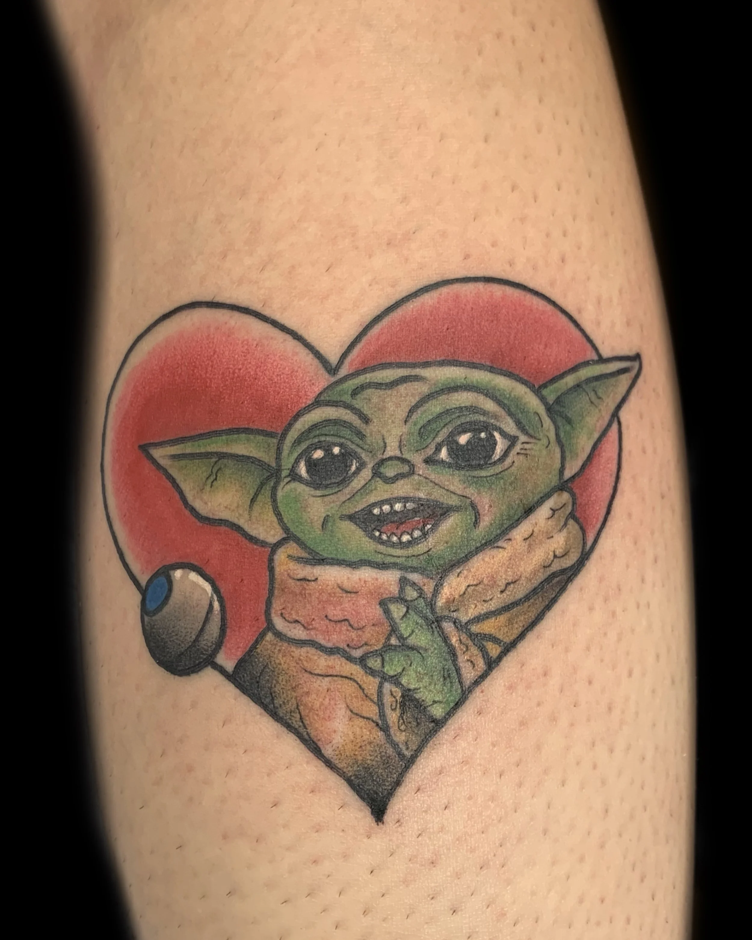 Tattoo of Baby Yoda inside a red heart with a black outline.