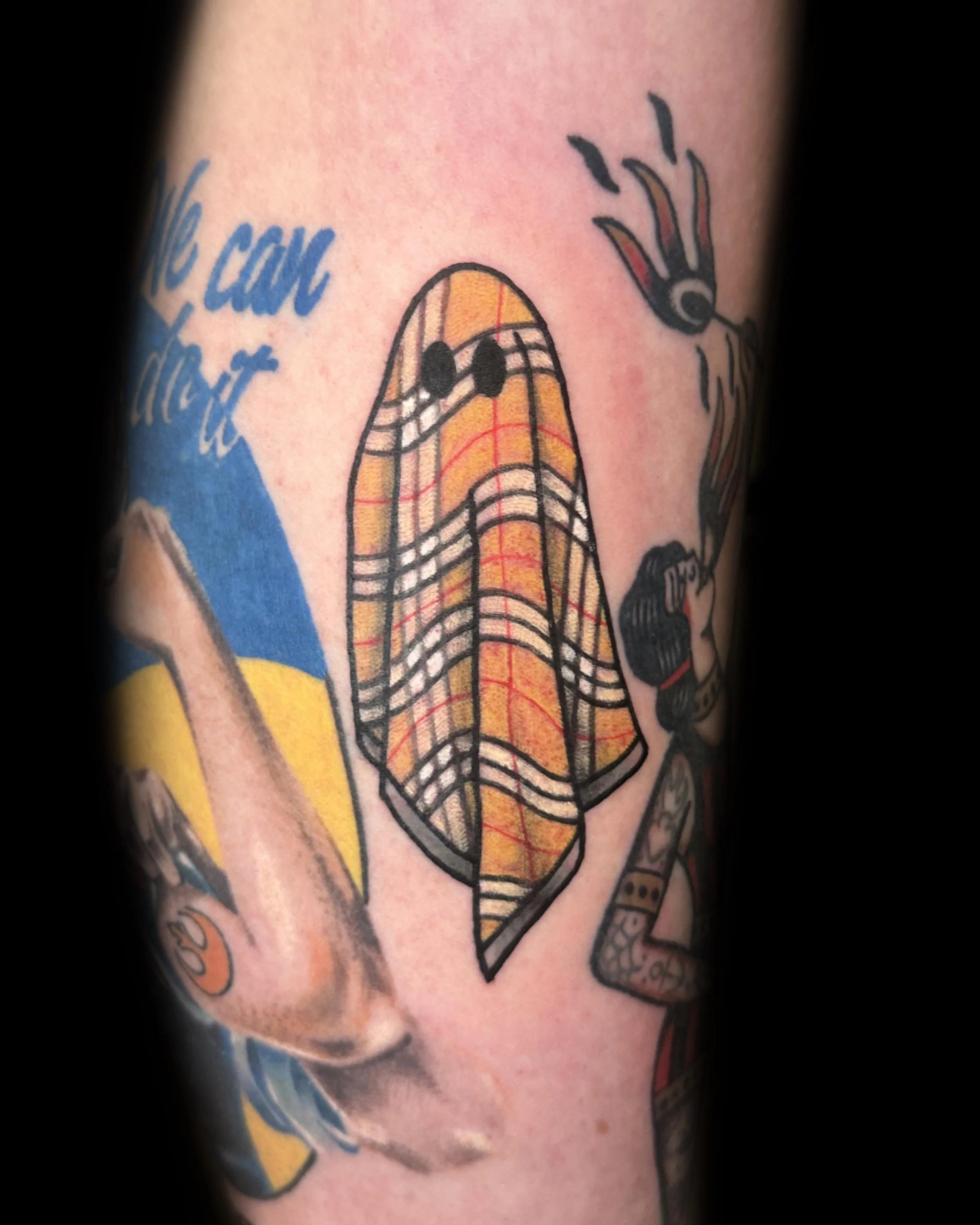 Tattoo of a guitar pick with tape and musical notes on a person's arm.