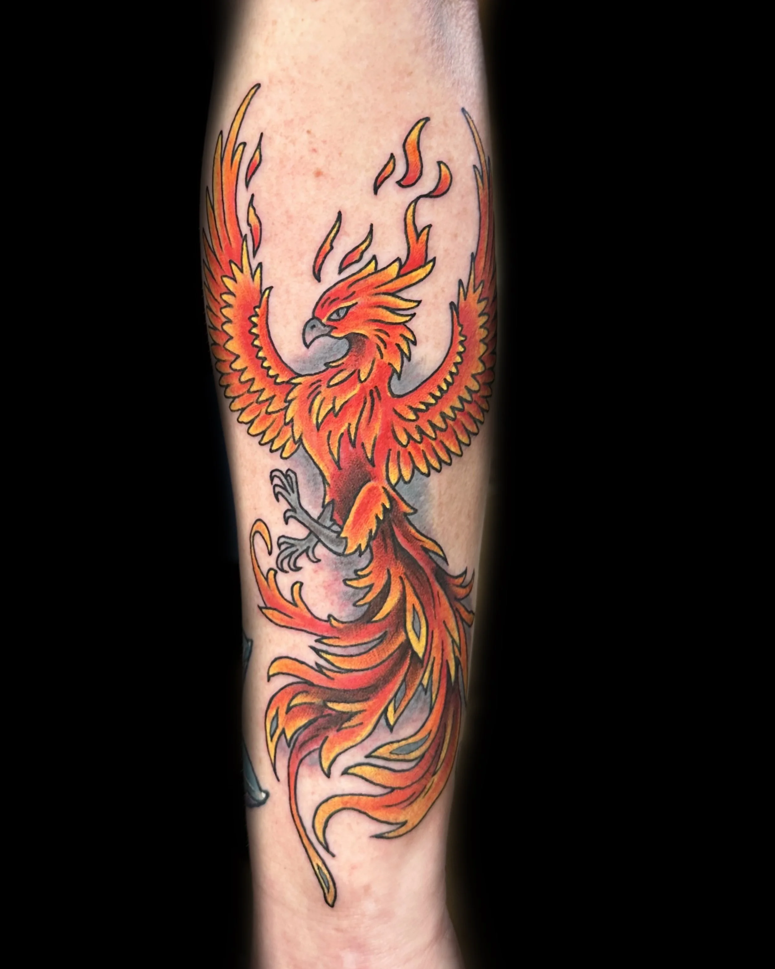 Colorful phoenix tattoo on person's forearm with flames and detailed feathers.