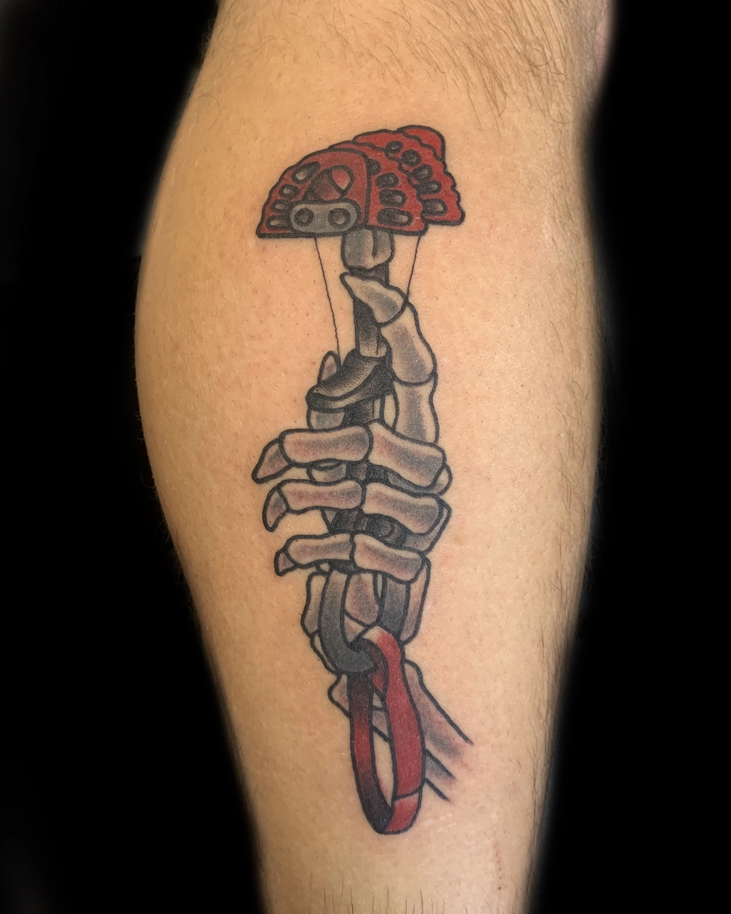 Tattoo of a human skeleton hand holding a mushroom with a red cap.