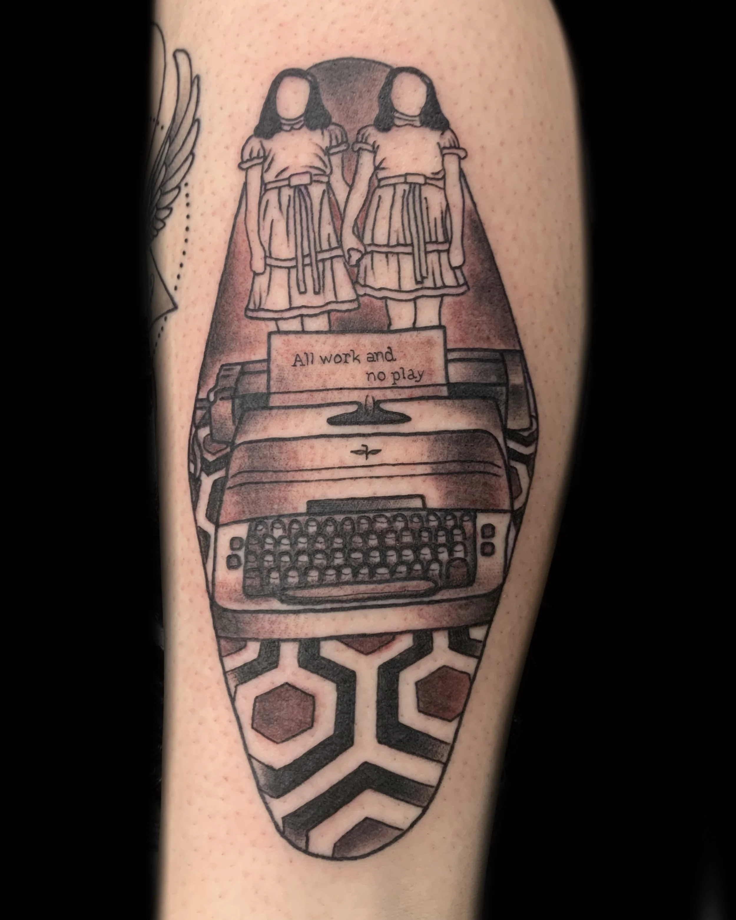 Stephen King's 'The Shinning' inspired tattoo of two girls holding hands, standing on a typewriter with a quote, and a patterned background.