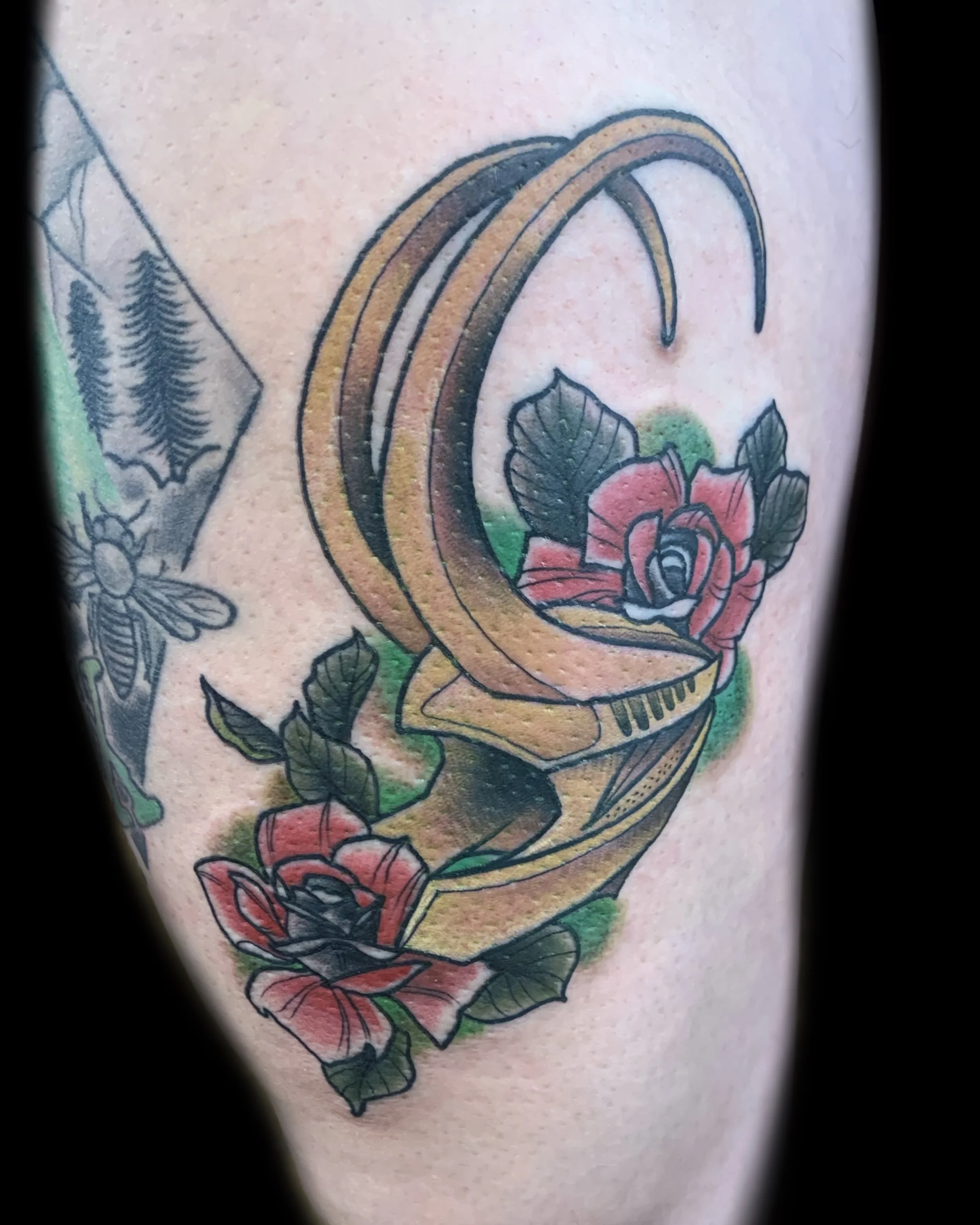 Tattoo of a golden telescope with pink and red roses and green leaves around it.