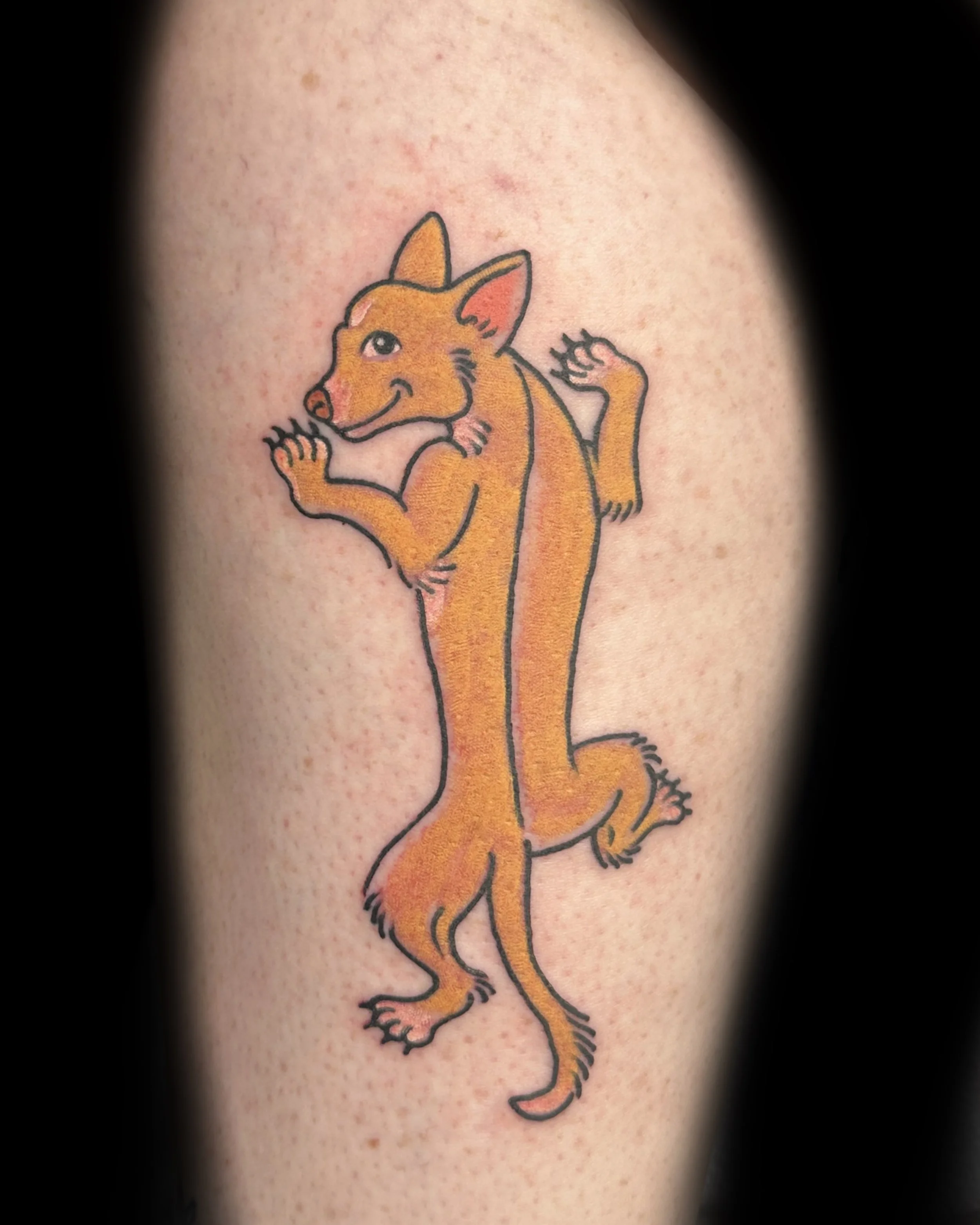 Colorful tattoo of a cartoon coyote wearing a small cowboy hat, standing on two legs, with a wink, and one arm bent, on human skin.