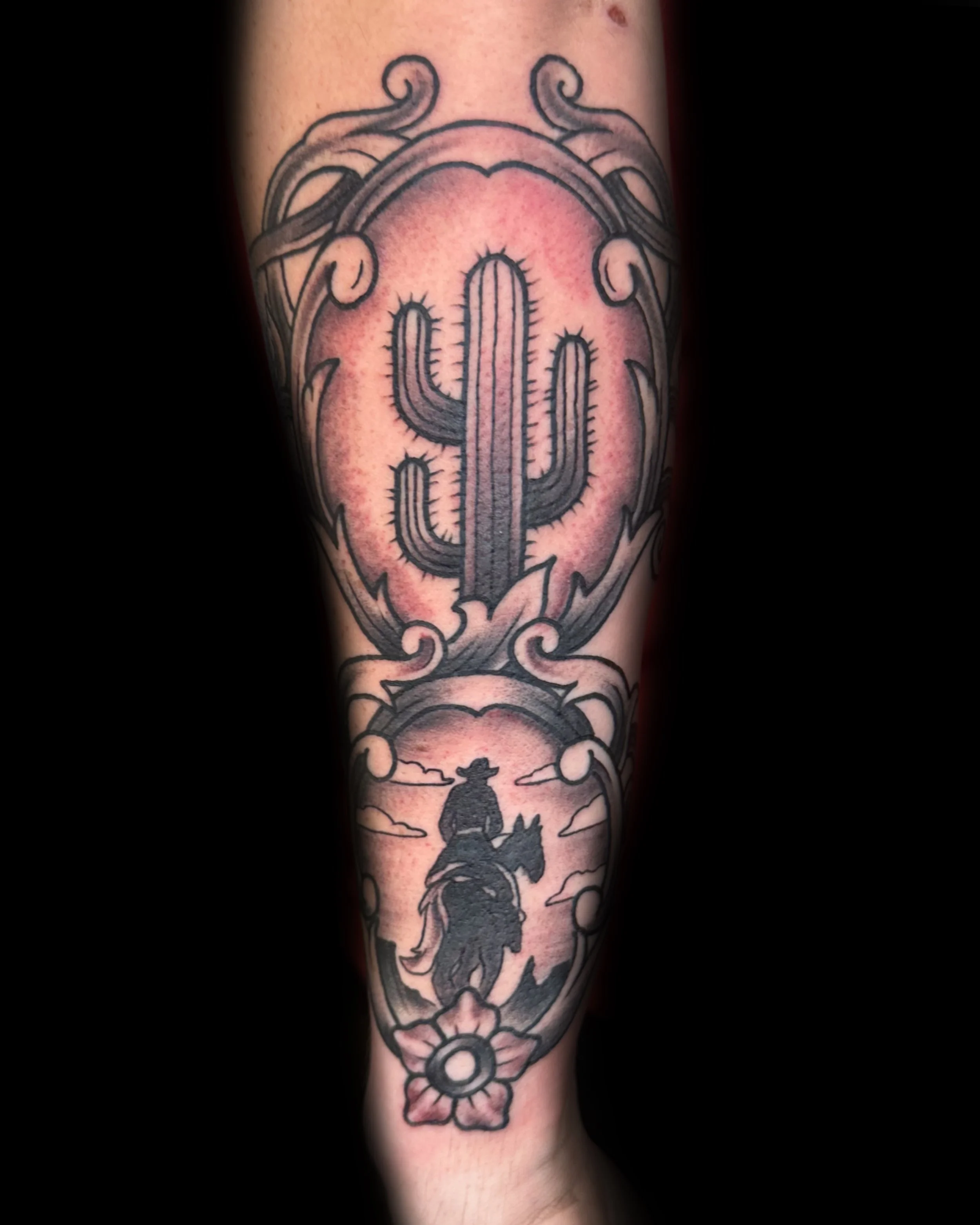 Tattoo of a cactus plant with decorative borders, and a silhouette of a cowpoke riding a horse with a sunset and clouds in the background.
