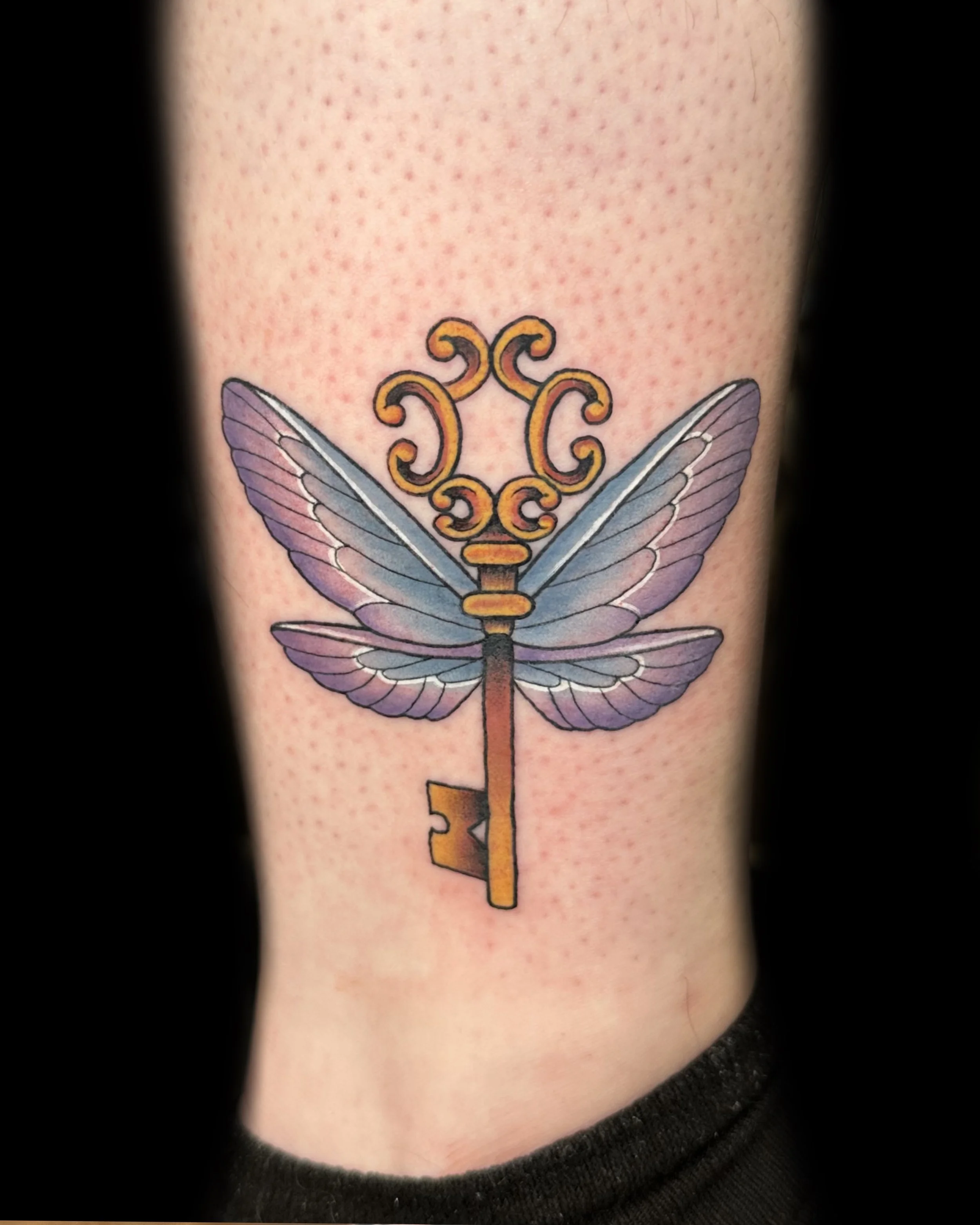 Colorful tattoo of a key with butterfly wings on the person's side.