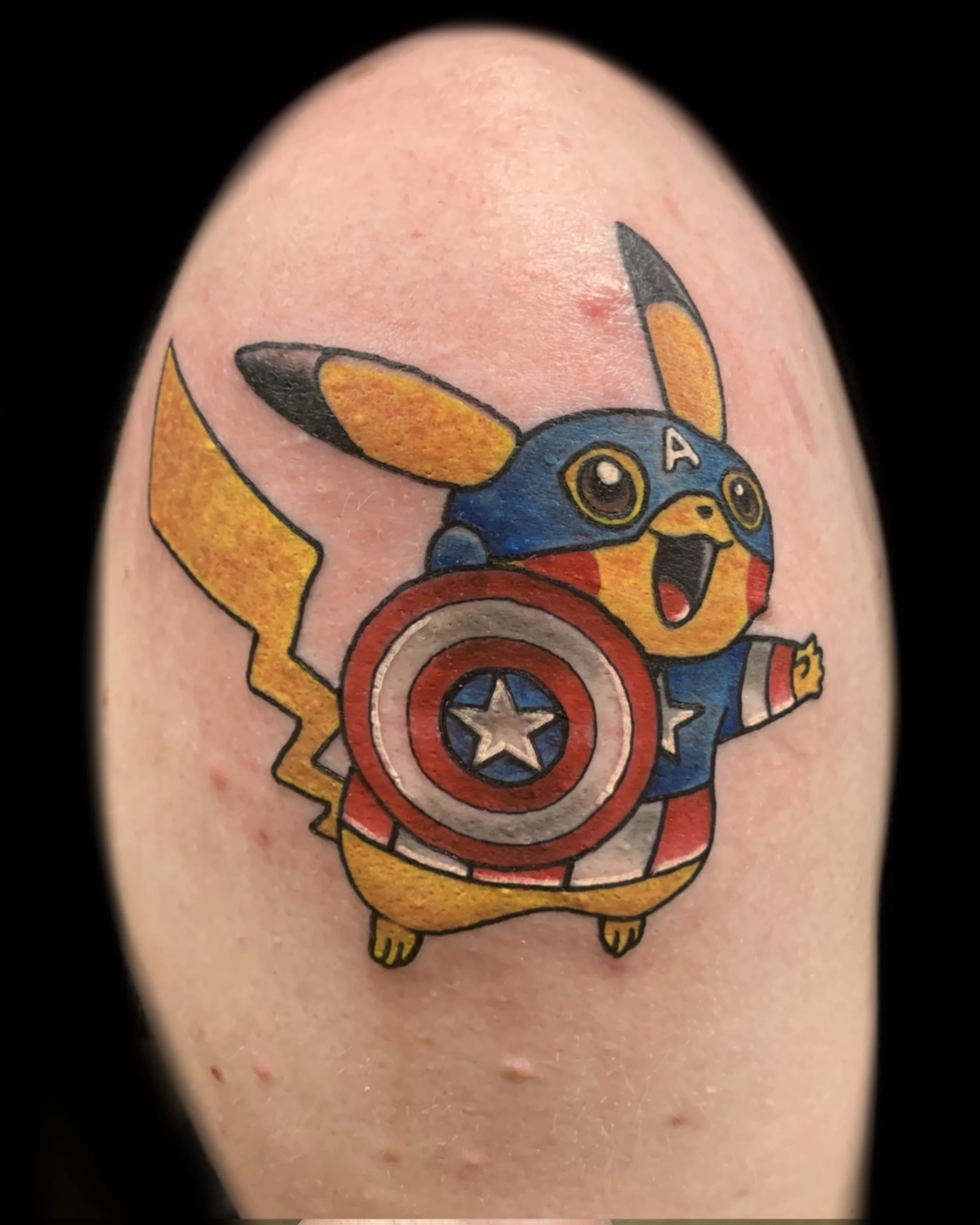 Tattoo of Pikachu dressed as Captain America, holding a shield with a star, on a person's skin.