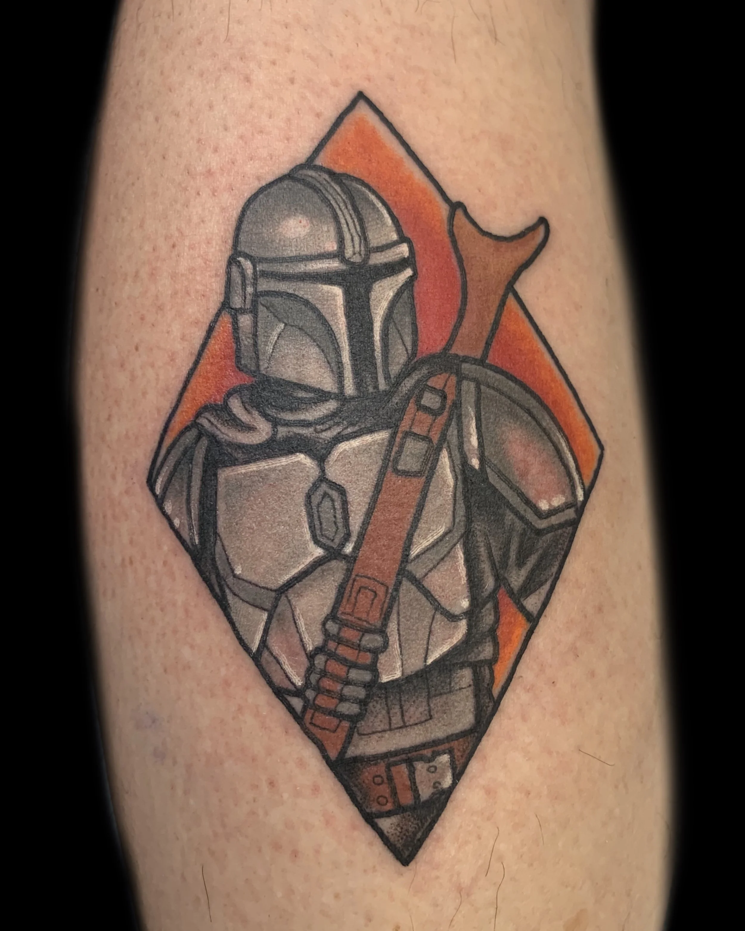 Tattoo of the Mandalorian character from Star Wars, with a background of a diamond shape and an orange triangle behind him.