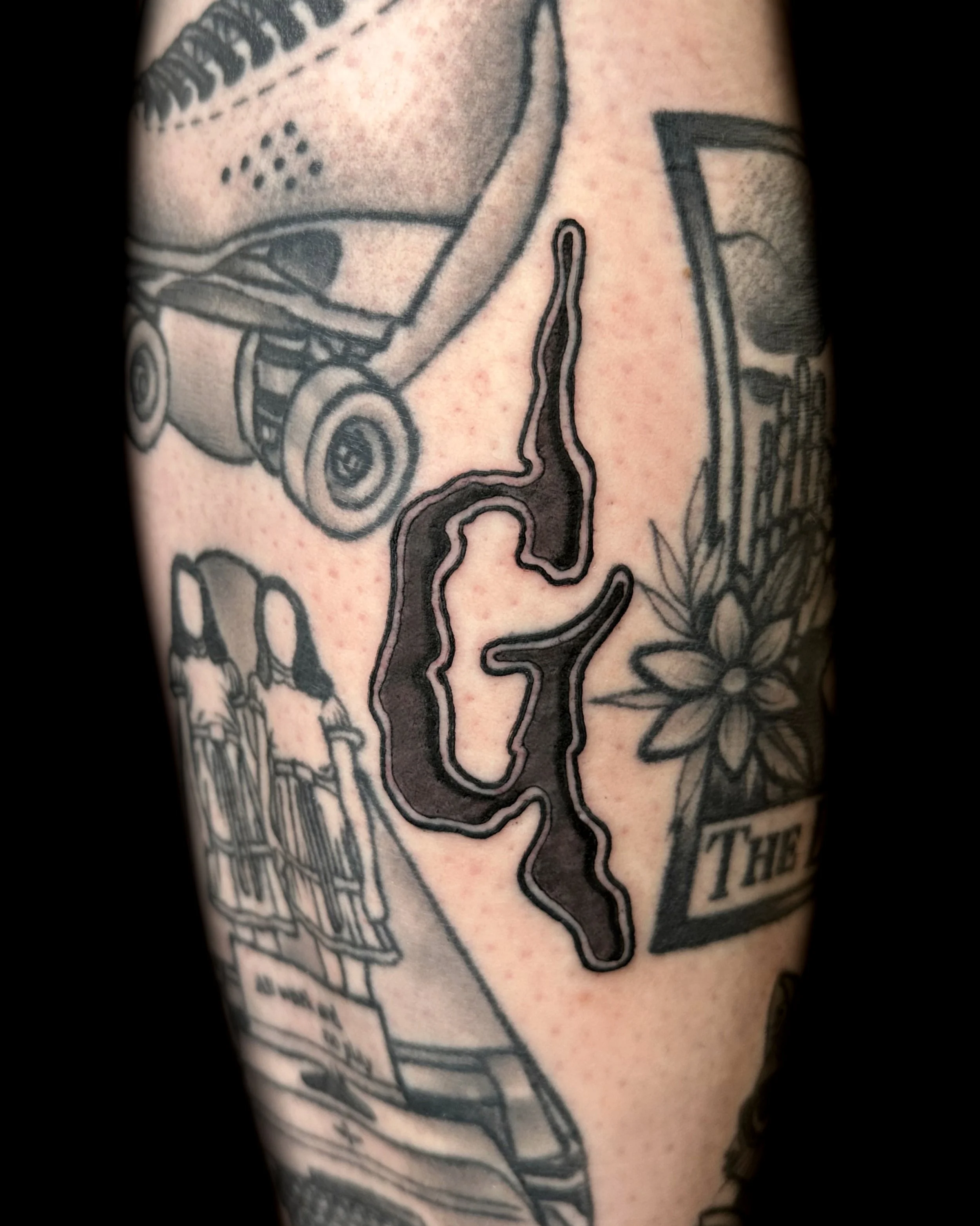 Tattoo of a map outline on skin, with adjacent tattoos including a flower with the word 'THE', a skateboard, and other designs.