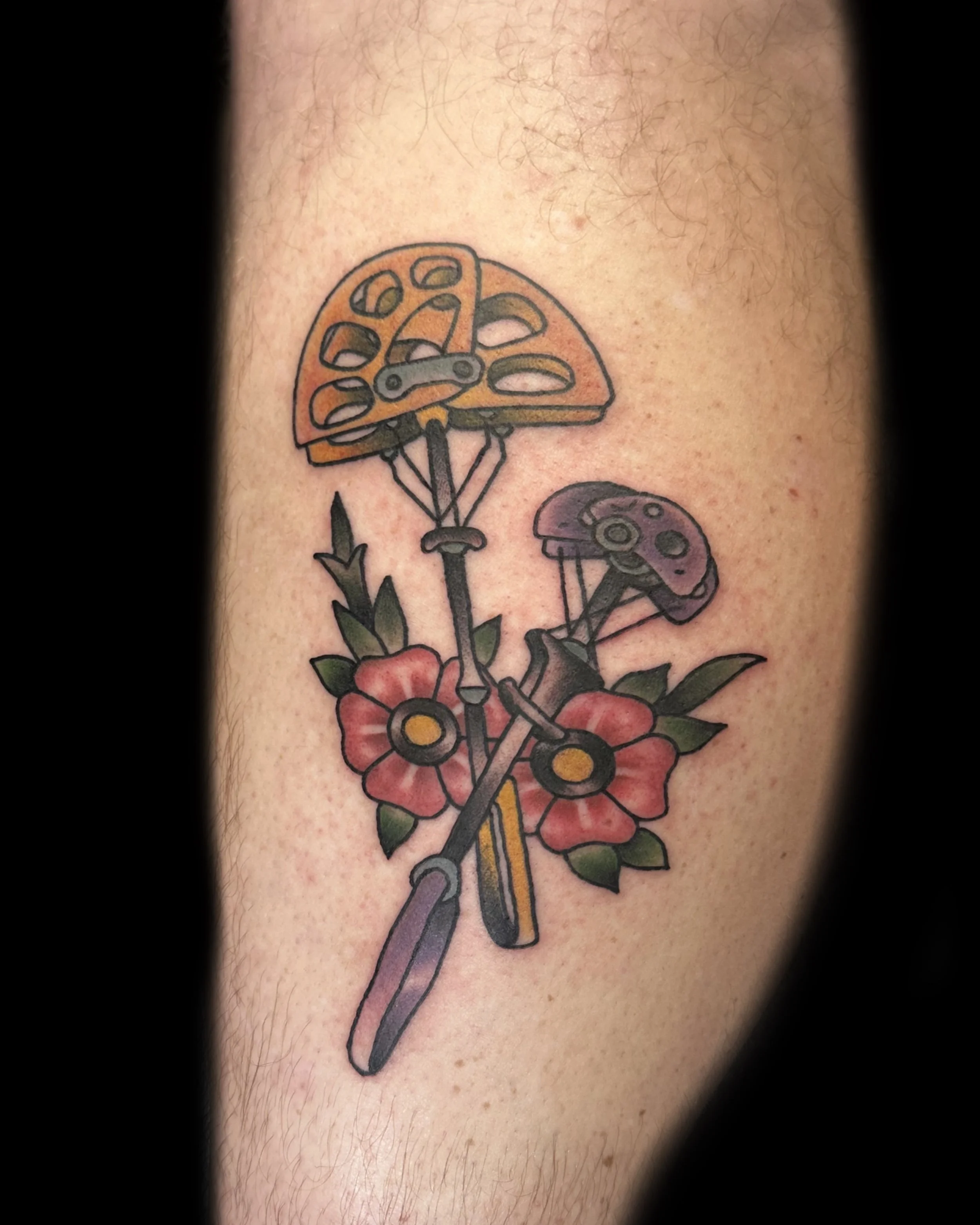 Colorful tattoo of two mushrooms, a flower, and gardening tools on skin.