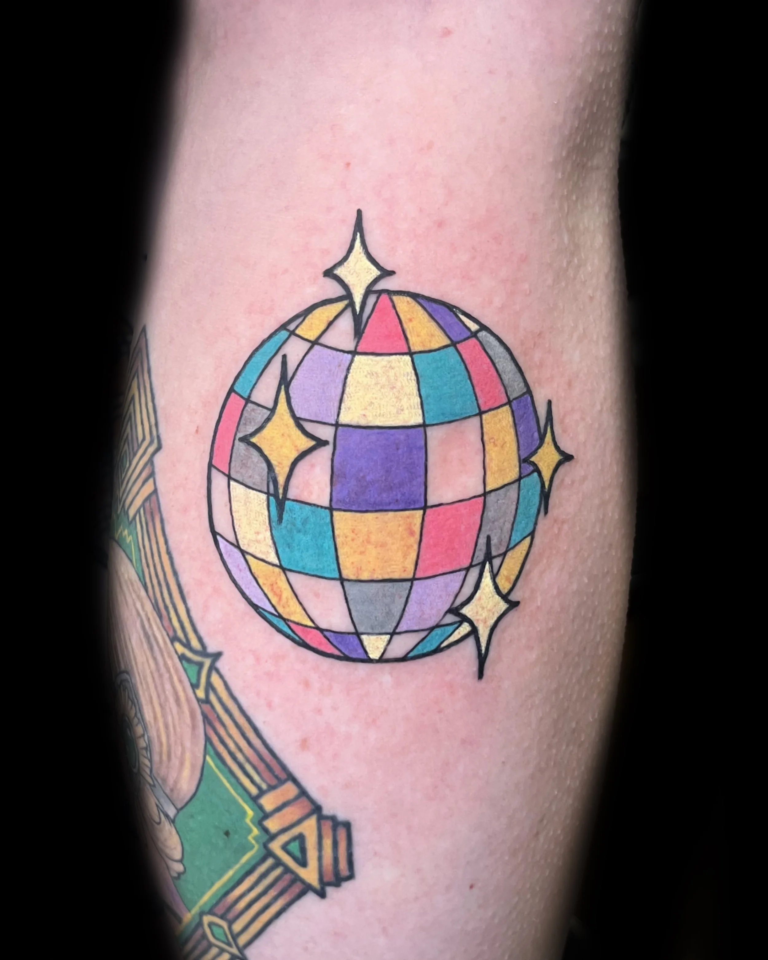 Colorful tattoo of a disco ball with stars on skin.