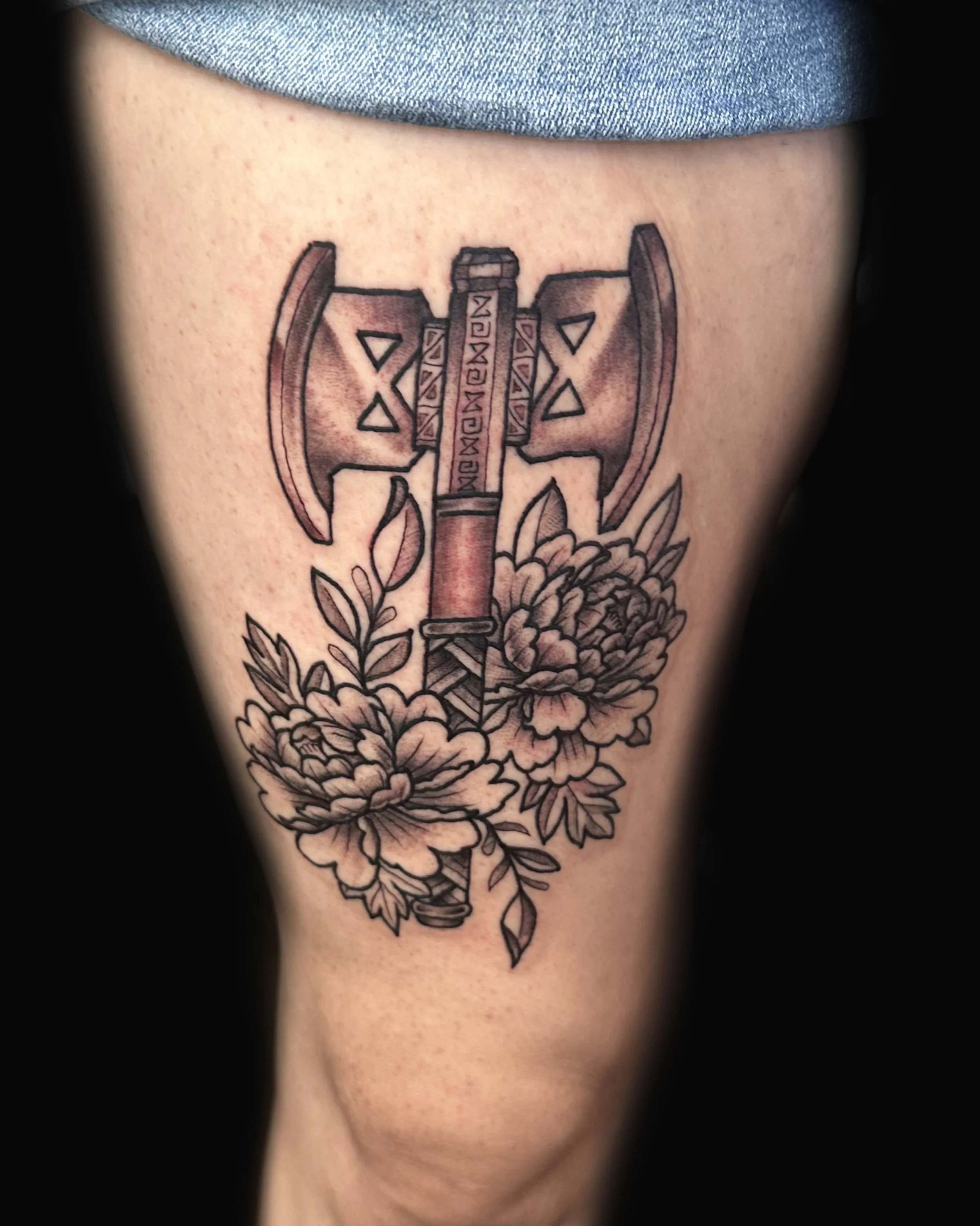 Tattoo of an axe with floral design, featuring detailed flowers and leaves.