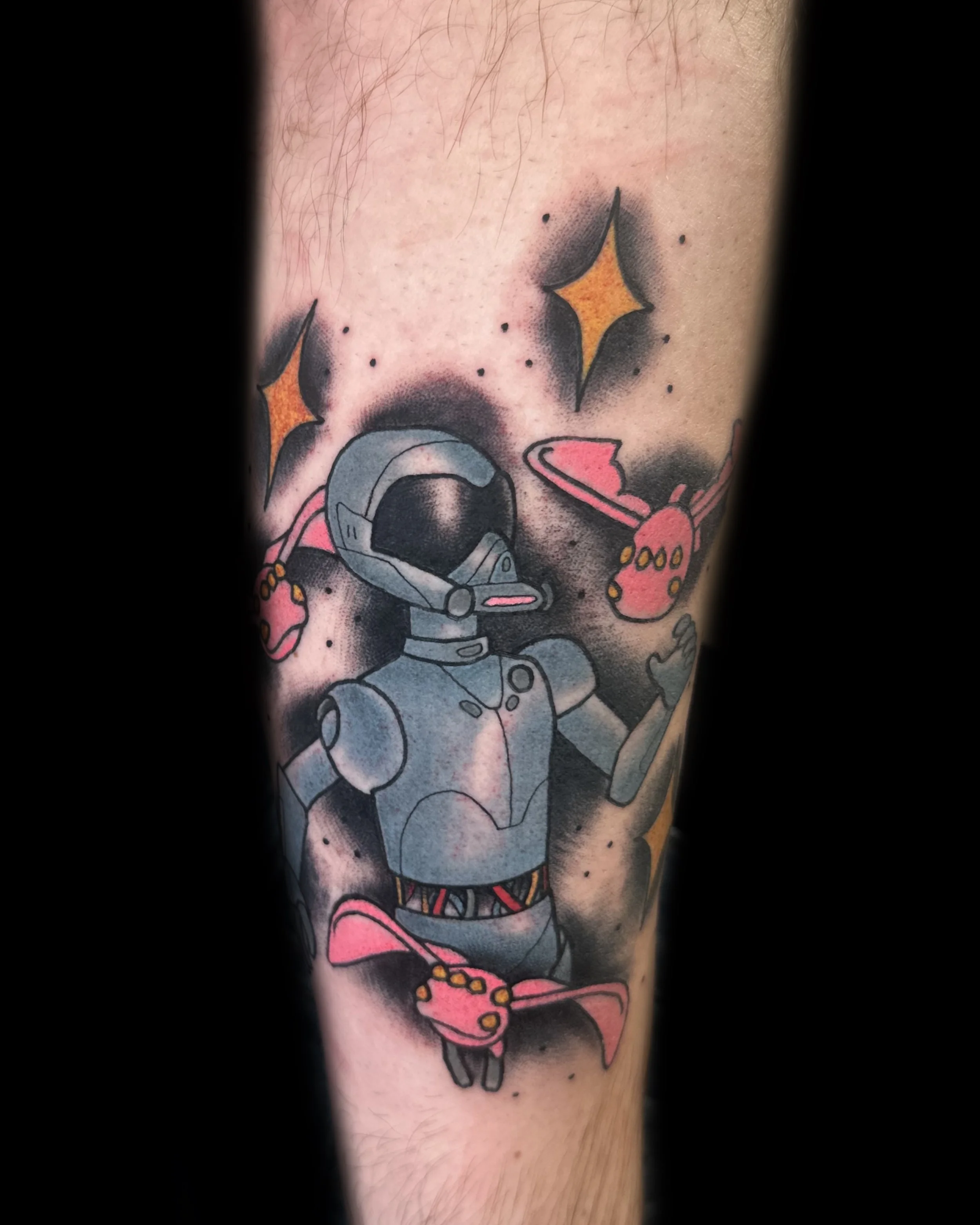 Tattoo of a robot astronaut surrounded by pink spacecraft and yellow stars on skin.