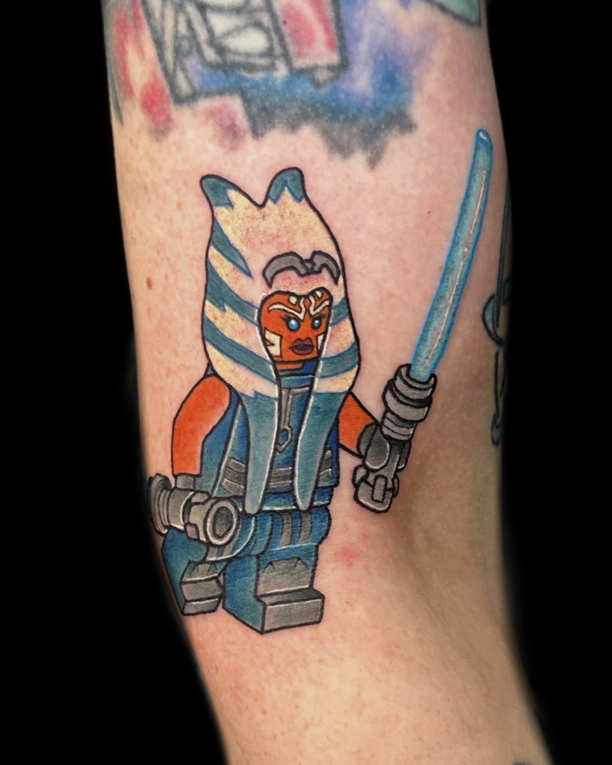 Tatoo of a LEGO Star Wars character, Ahsoka Tano, with a shipo and a Jedi lightsaber.