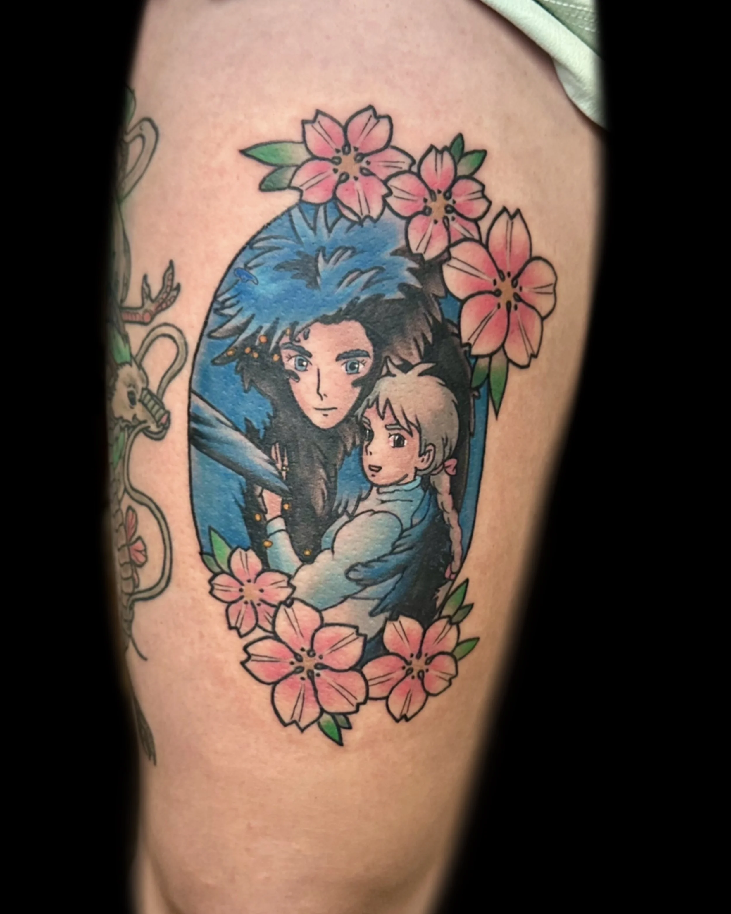 Tattoo of two animated characters, a girl with braided hair and a boy with spiky hair, surrounded by pink flowers.